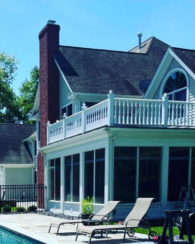 Sunroom with a white deck railing, attached to a brick chimney house, overlooking a pool with lounge chairs.
