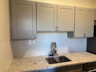 Modern kitchen area featuring light gray cabinets, a white herringbone backsplash, and a marble-patterned countertop.