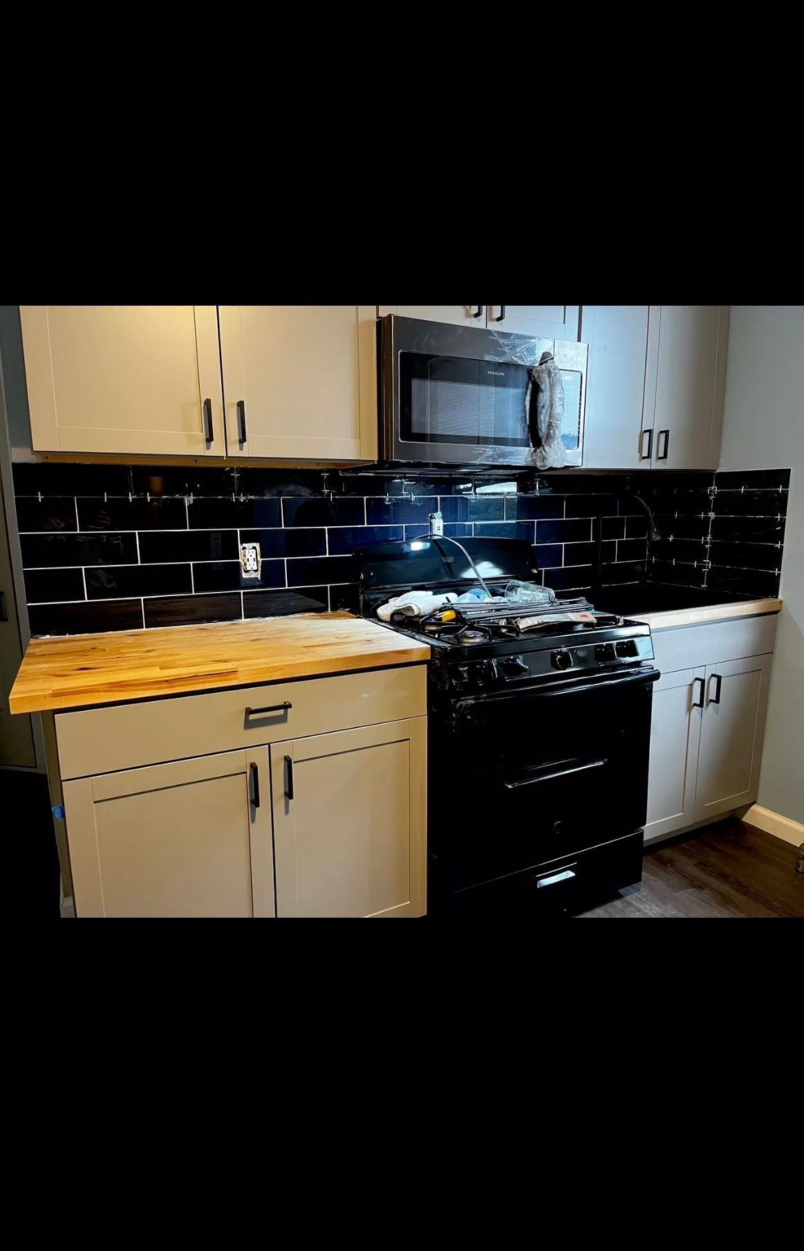 Kitchen featuring light-colored cabinets, a butcher block countertop, a black gas stove with microwave, and black tiles.