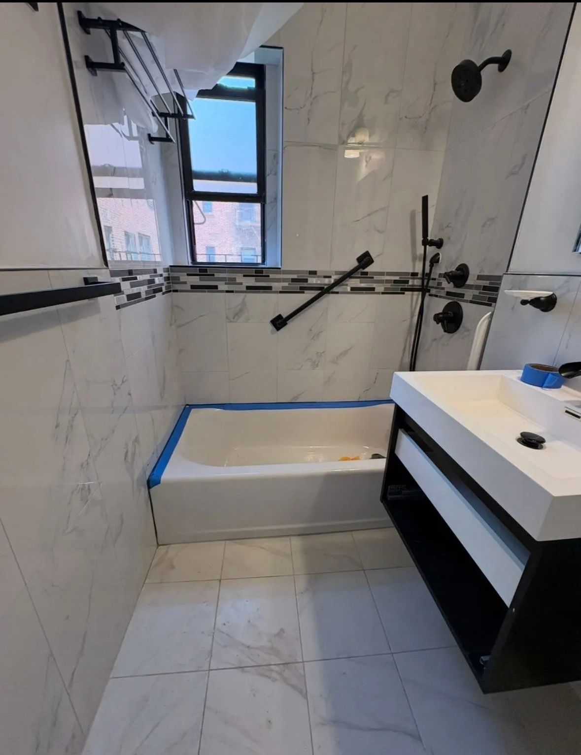 A modern white kitchen with wood floors, stainless steel appliances, and a patterned tile backsplash.