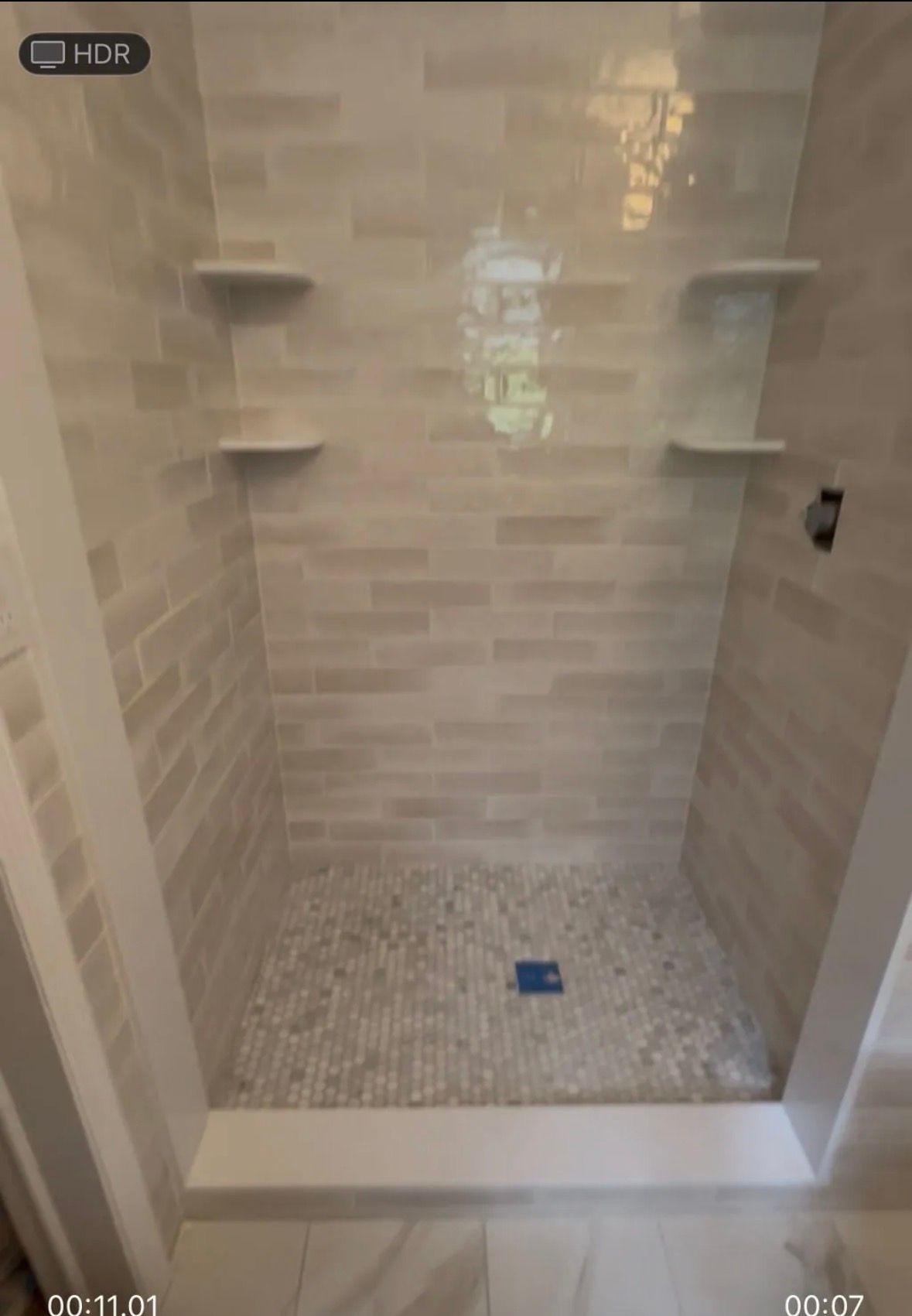 A walk-in shower with light, rectangular wall tiles, a pebble-stone floor, and four built-in corner shelves.