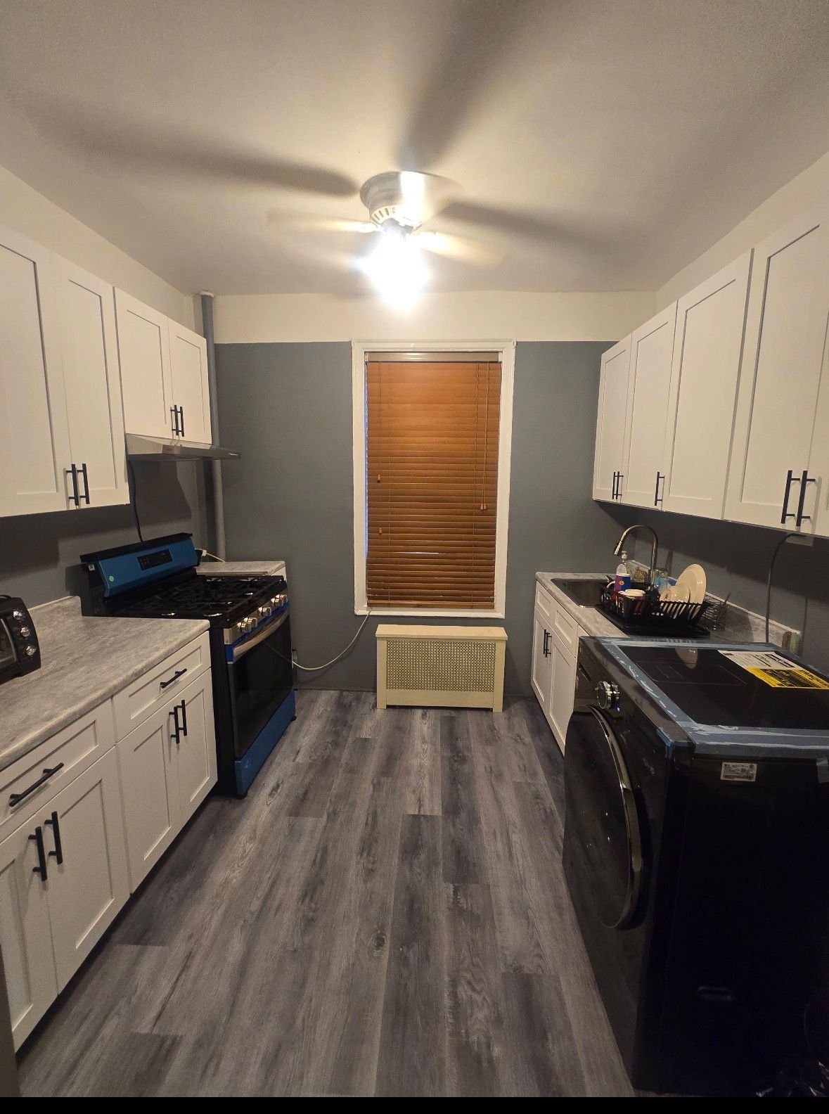 Modern kitchen with white cabinets, dark gray walls, stainless steel appliances, and hardwood floors.