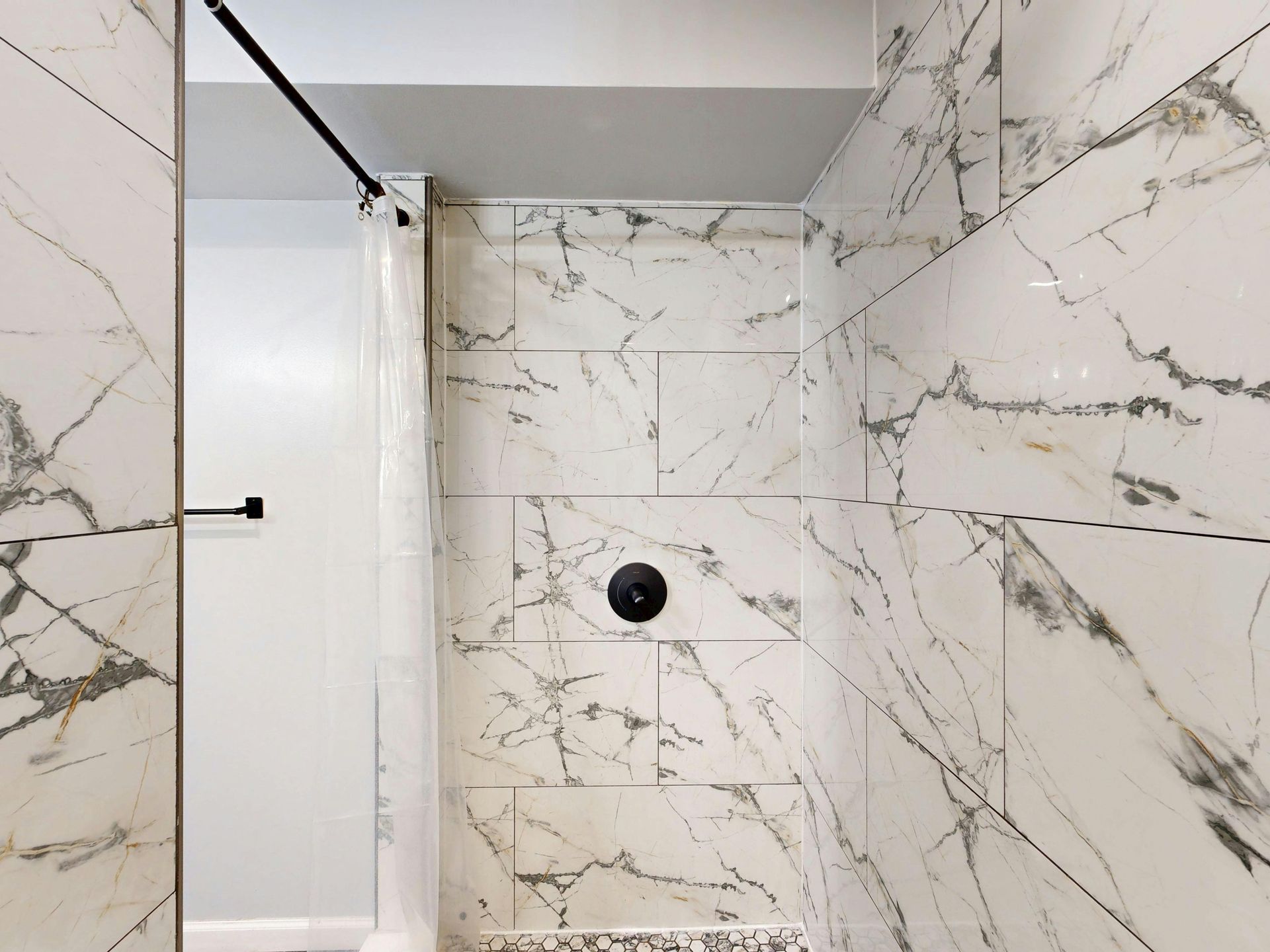 A shower stall with white marble-patterned wall tiles and black plumbing fixtures.