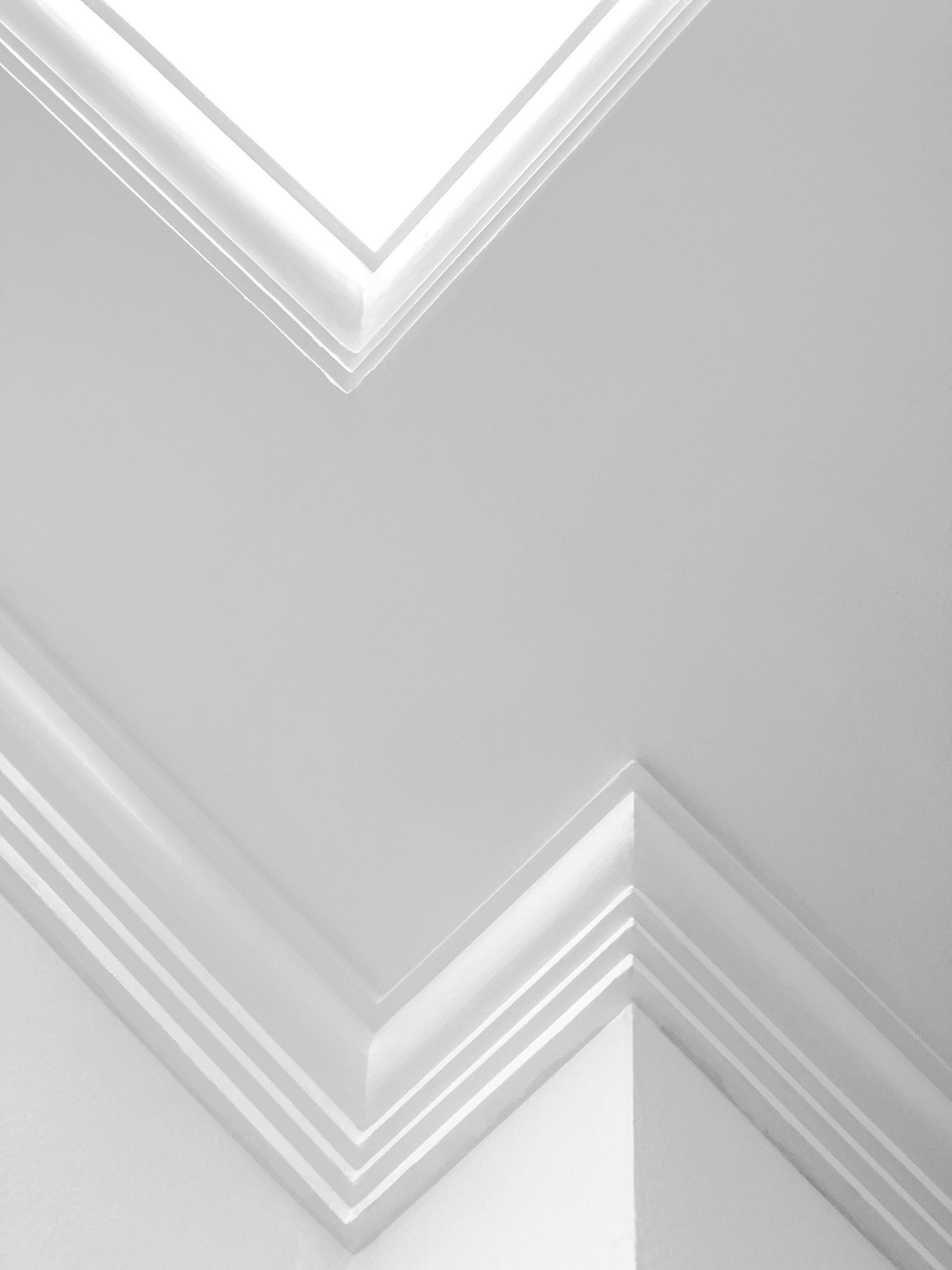 An upward-angled view of white ceiling molding forming geometric corners and angles against a plain, light background.