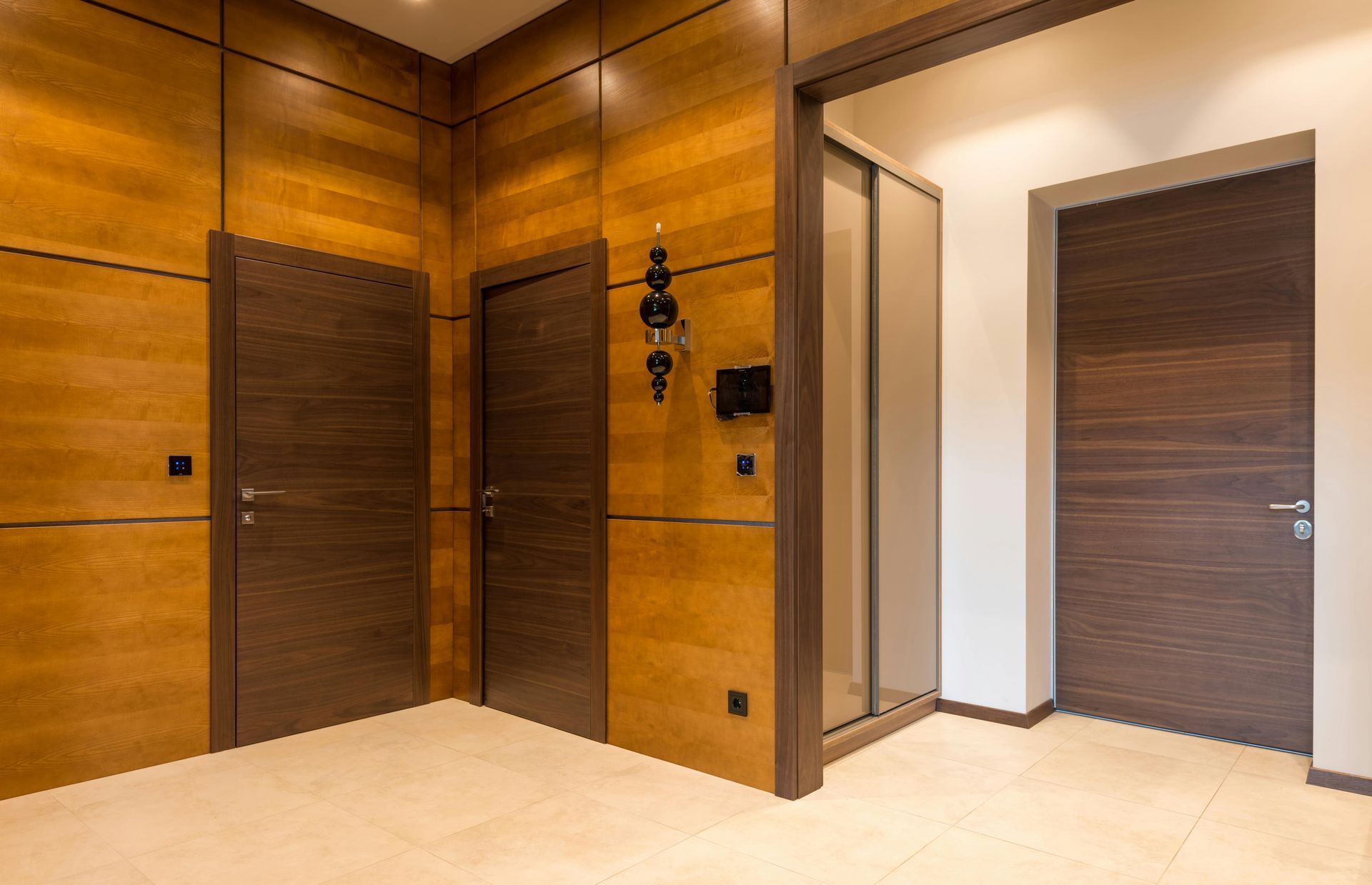 A modern hallway with light beige tile floors, wood-paneled walls, and three dark wood interior doors.
