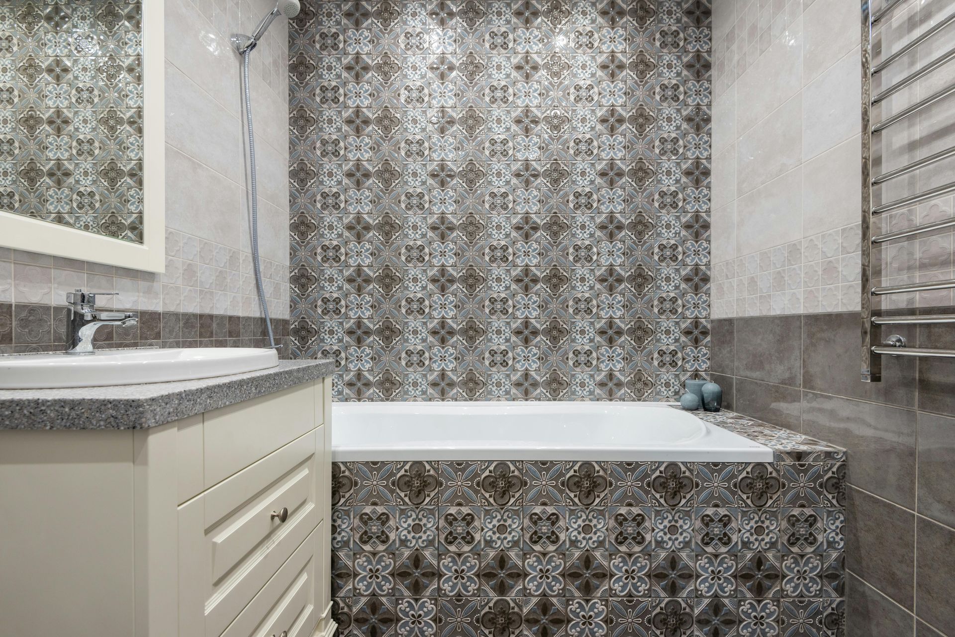 A bathroom featuring a white vanity, a white bathtub, and walls covered in brown and white patterned decorative tiles.