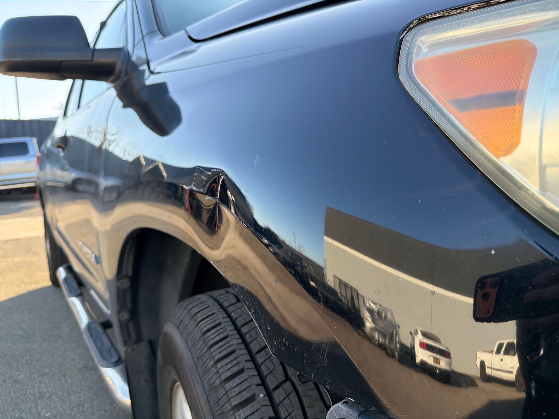 Black truck with a dented front fender and headlight.