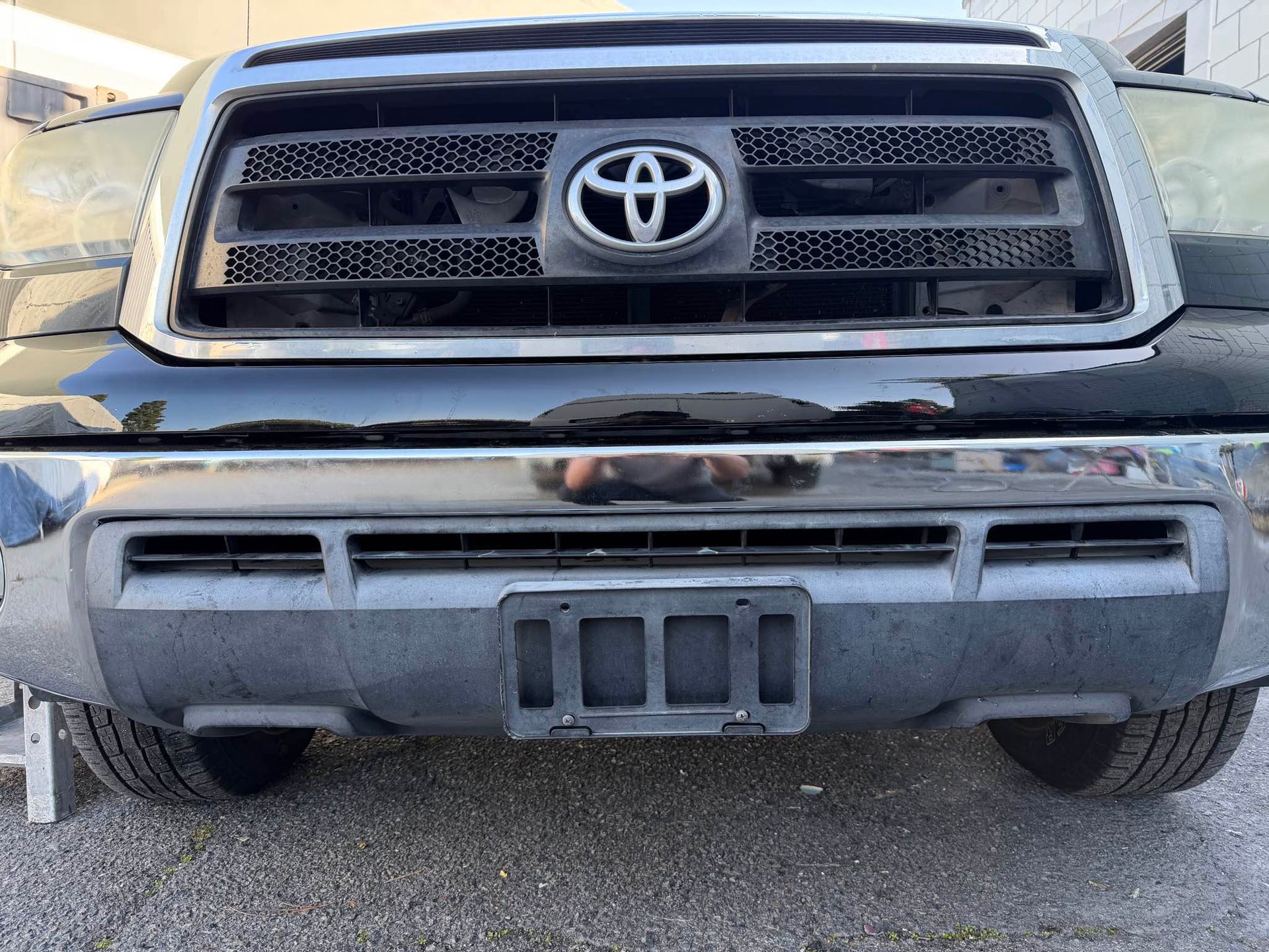 Black Toyota truck front with grill, emblem, and bumper, parked on pavement.