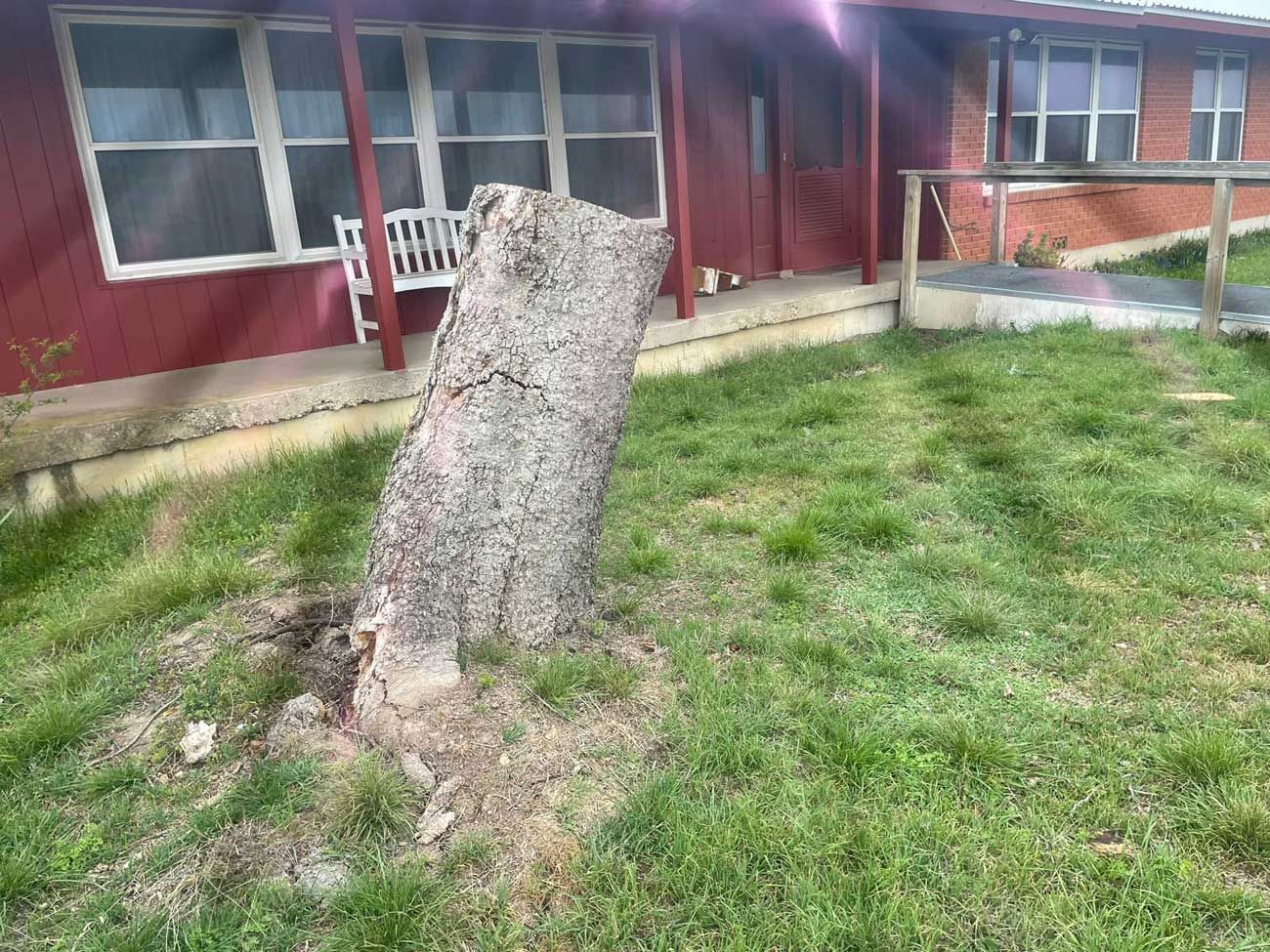 A large tree stump is in the grass in front of a red house.