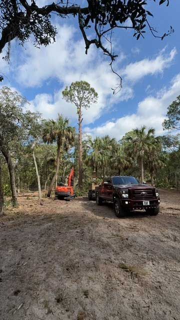 A red truck is parked in a dirt lot next to an orange excavator.