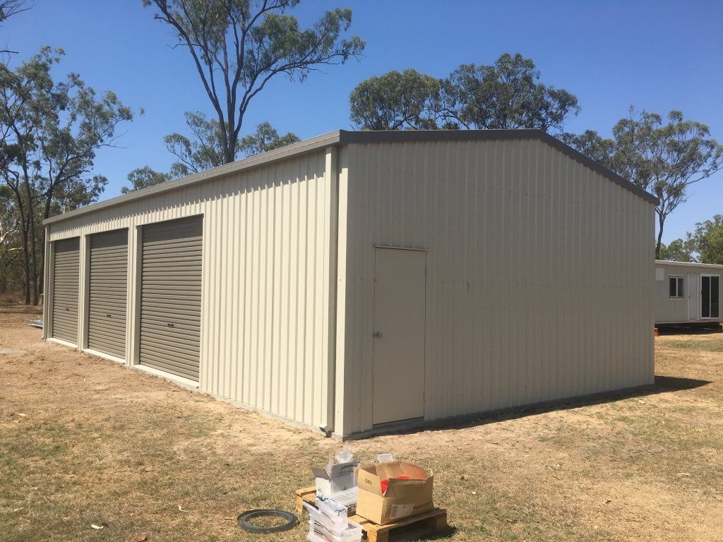 A Large White Metal Building With Three Garage Doors is Sitting in the Middle of a Field — Shedquarters In Kirwan, QLD