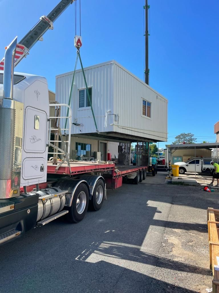 A Truck With a Crane Attached to It is Carrying a Building — Shedquarters In Kirwan, QLD