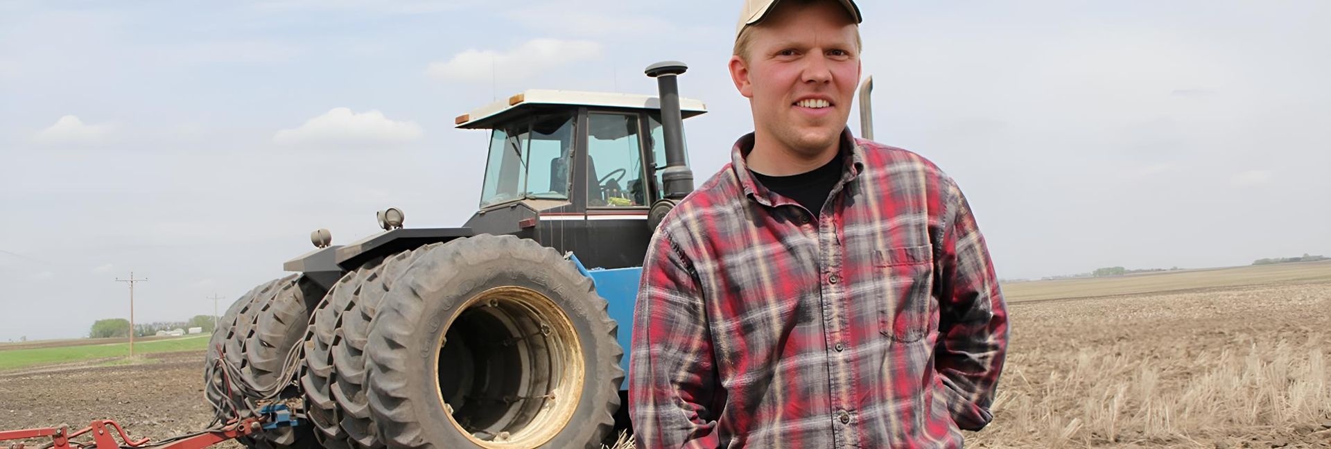 A Man In A Plaid Shirt Is Standing In Front Of A Tractor In A Field — Shedquarters In Kirwan, QLD