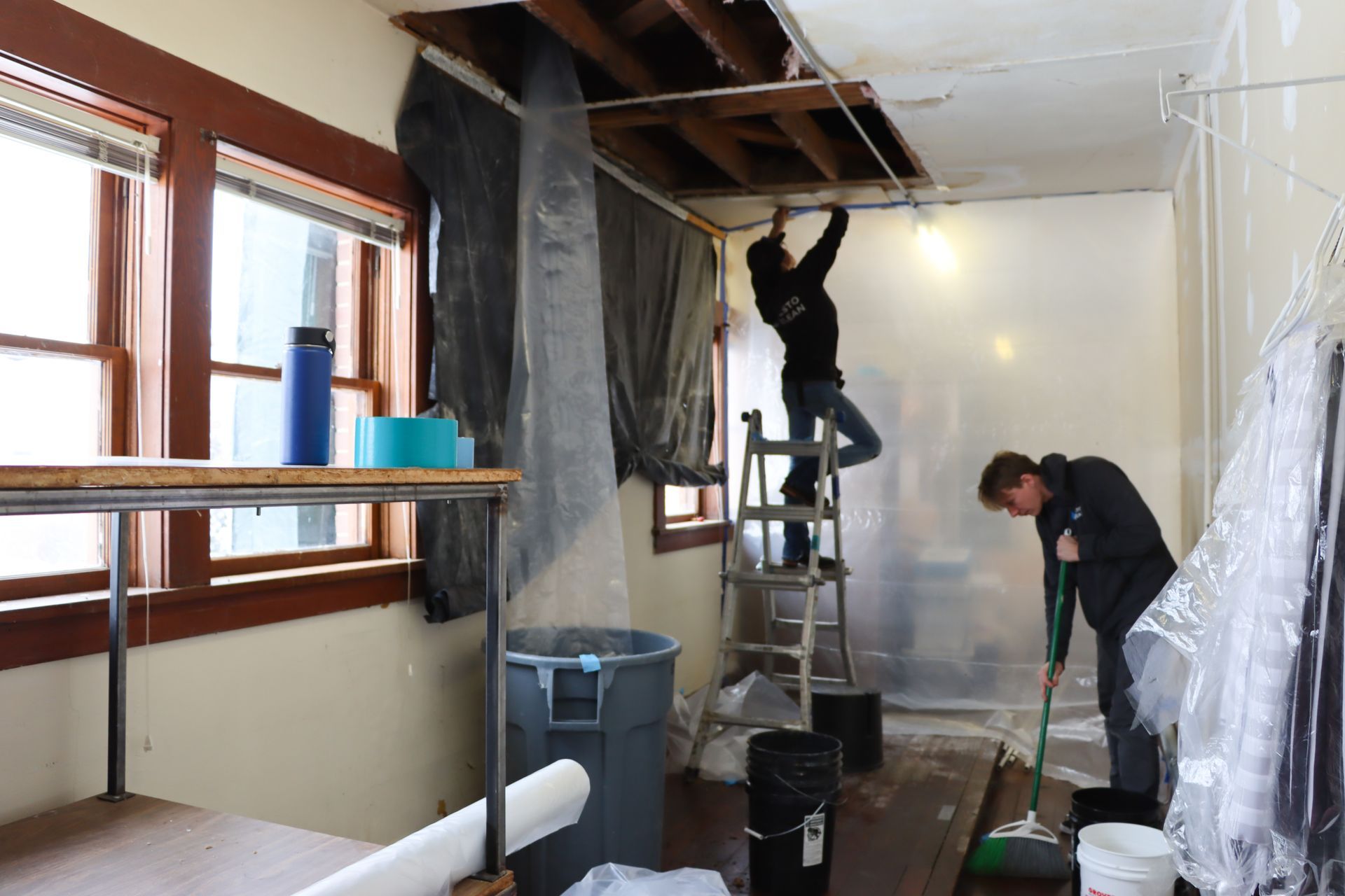 Two men are working on the ceiling of a room.