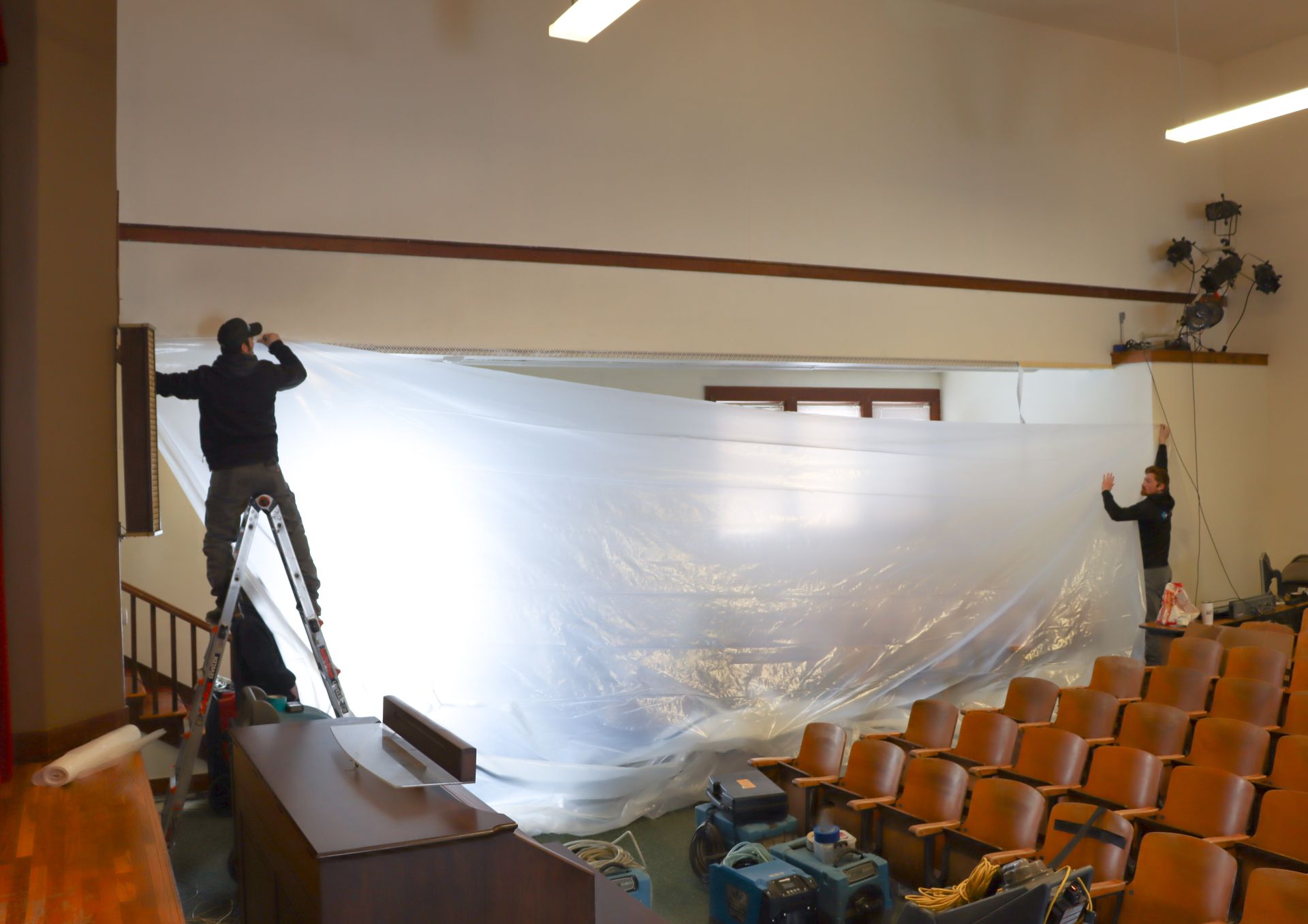 a man on a ladder is covering a wall with plastic .