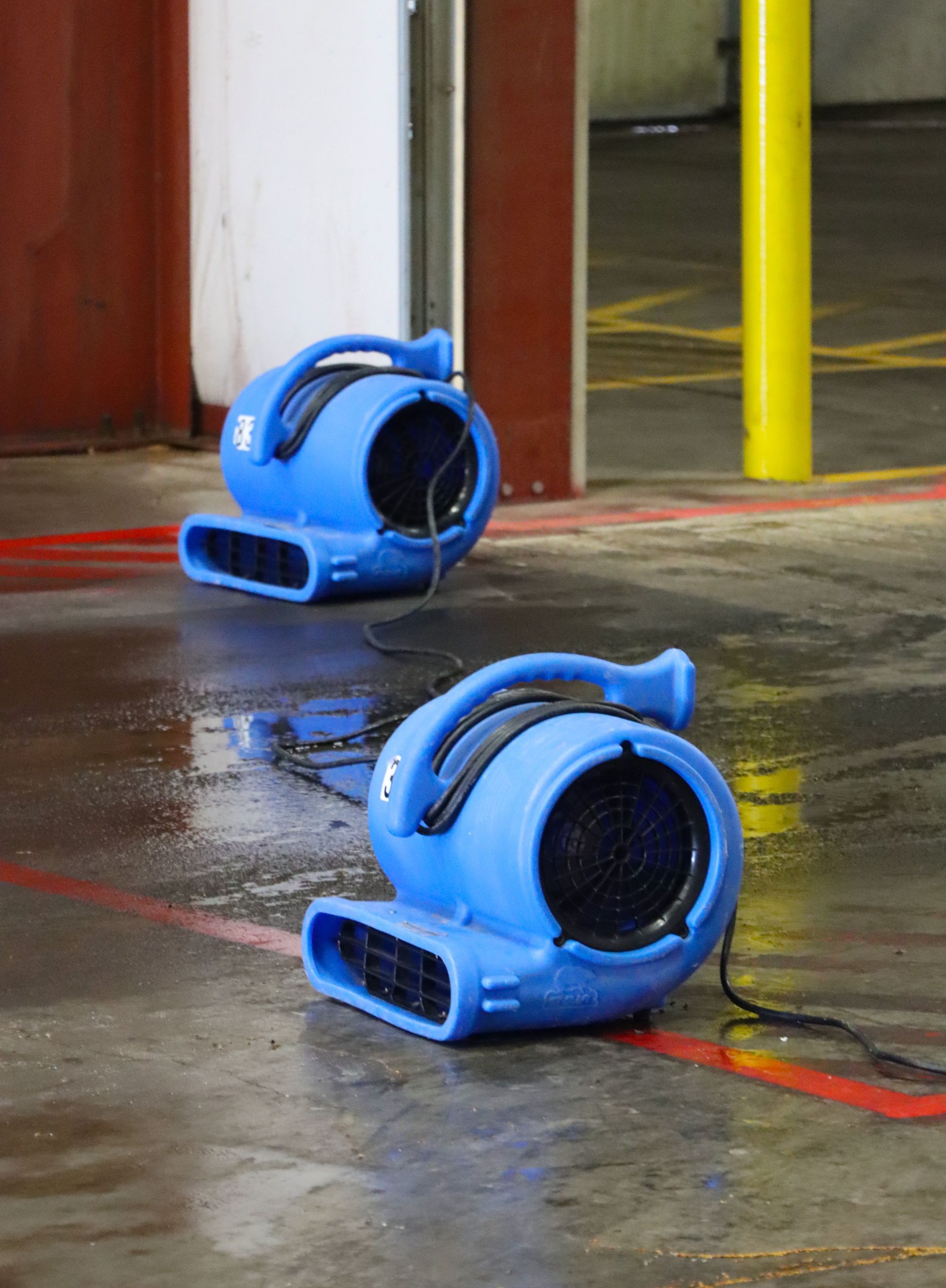 Two blue fans are sitting on the floor of a building.