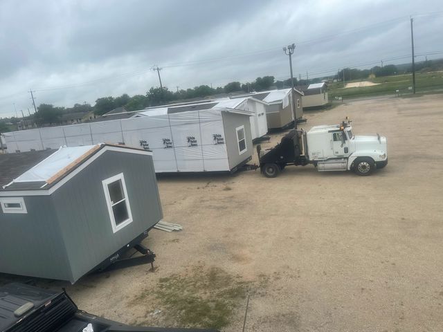 A white truck is towing a row of sheds in a dirt lot.