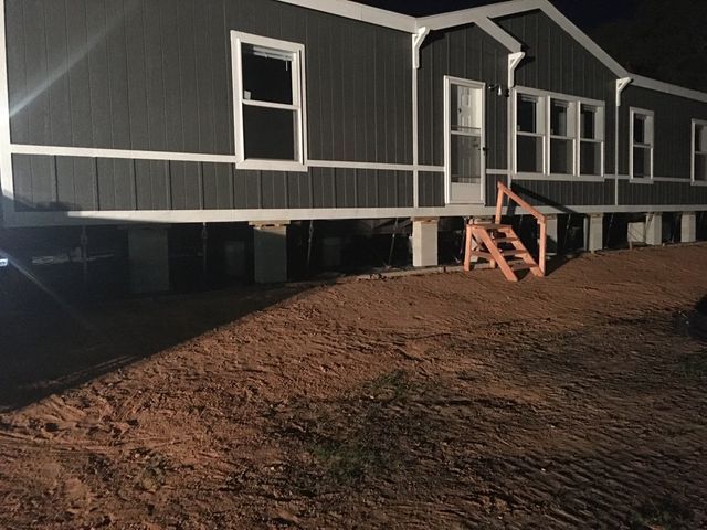 A mobile home is sitting on stilts in a dirt field at night.
