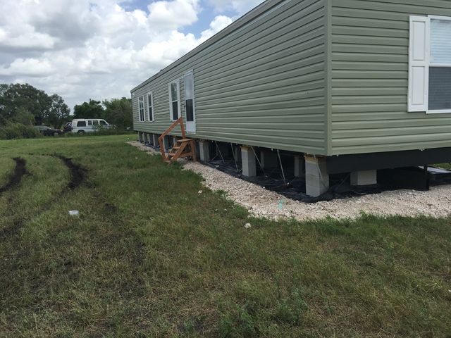 A mobile home is sitting on stilts in a grassy field.
