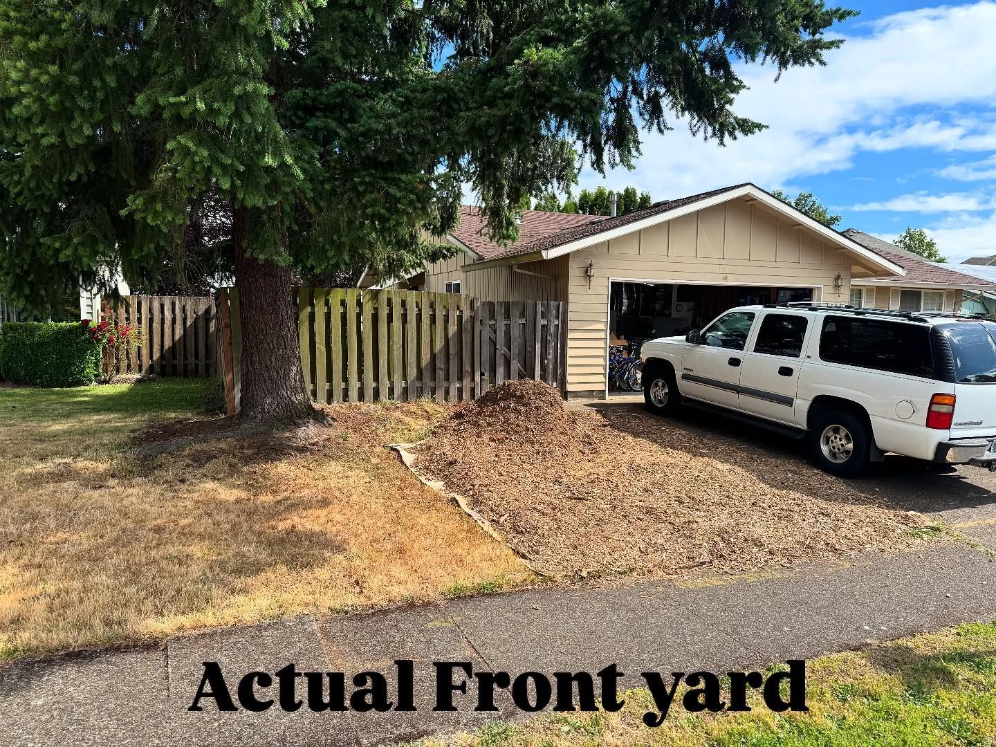 Front yard of a beige house with dry grass, a fence, and a white SUV parked in front of a garage.