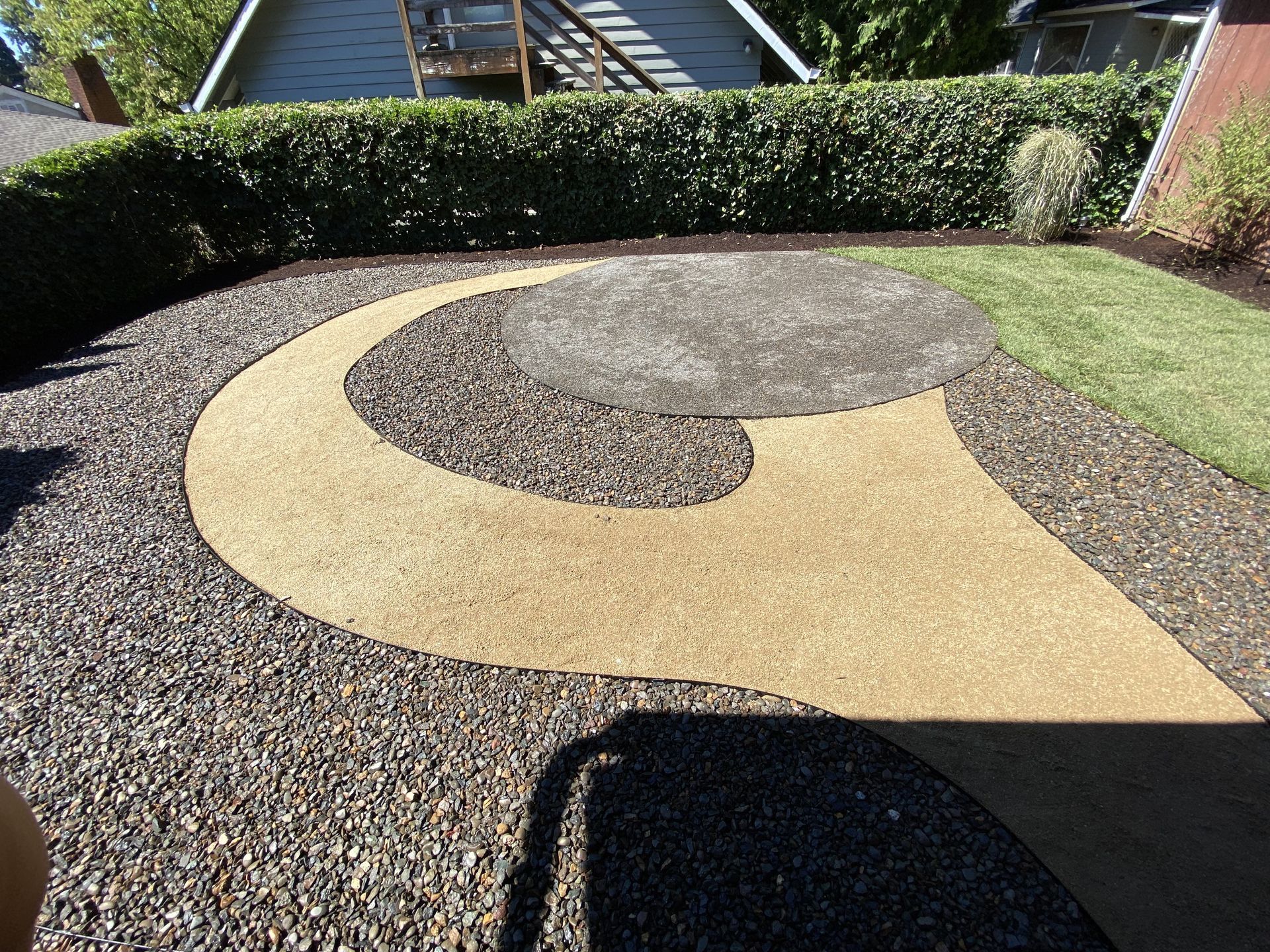A gravel and concrete landscaped backyard with a curved path. A gravel and concrete landscaped backyard with a curved path.