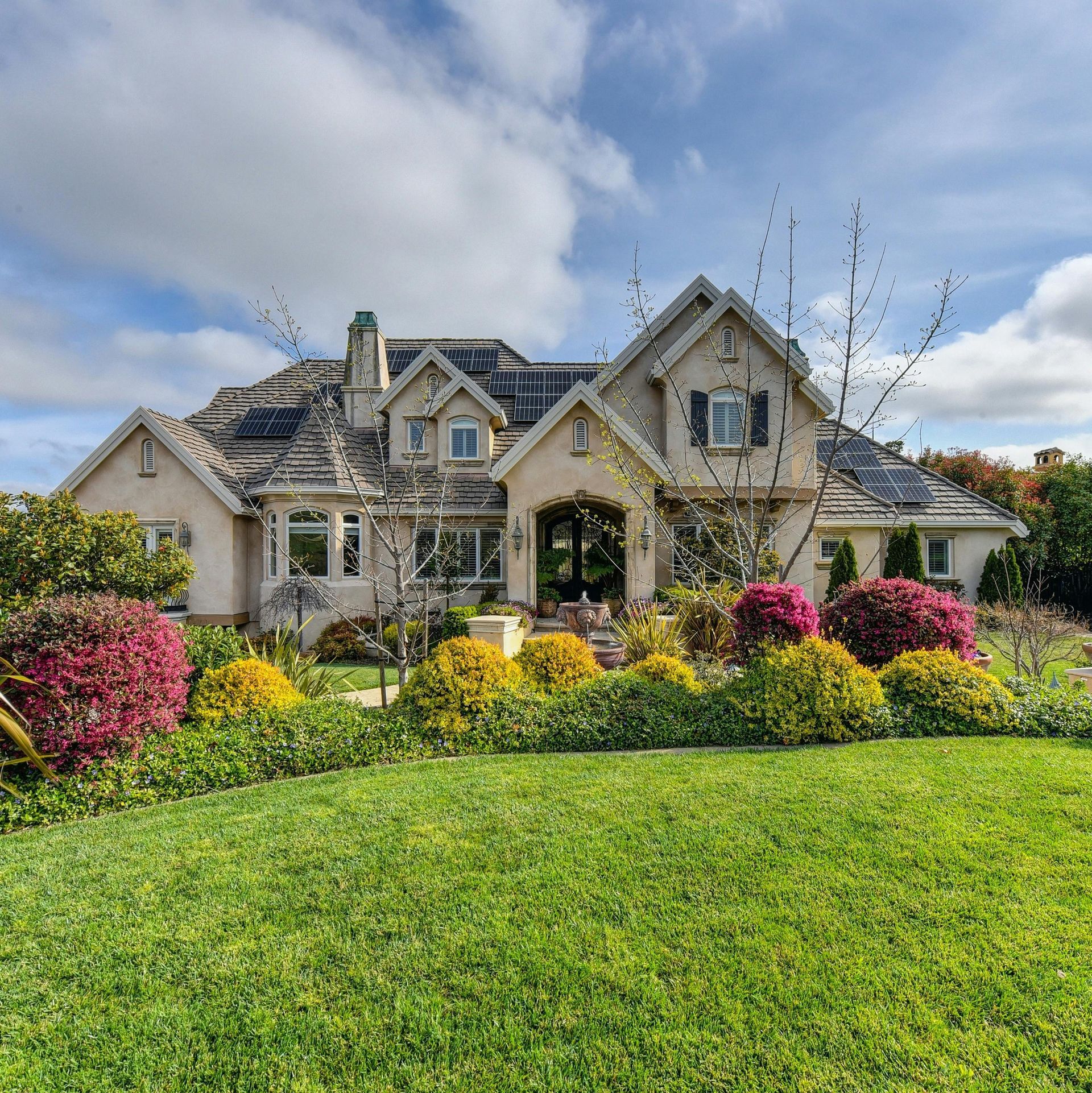 Elegant house with lush green lawn and colorful bushes under a partly cloudy sky.