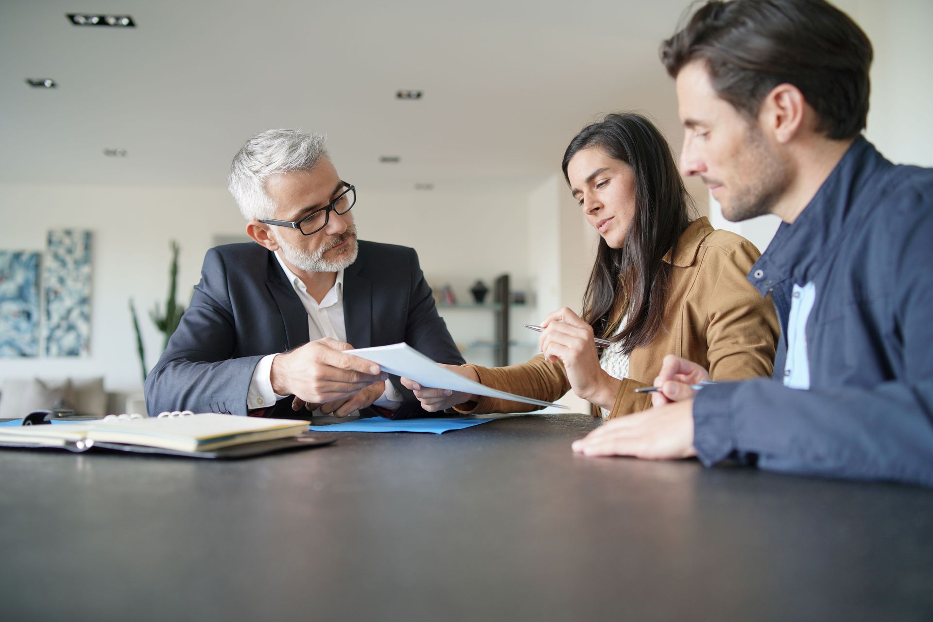 A professional advisor presents a document to a couple across a desk during a consultation.