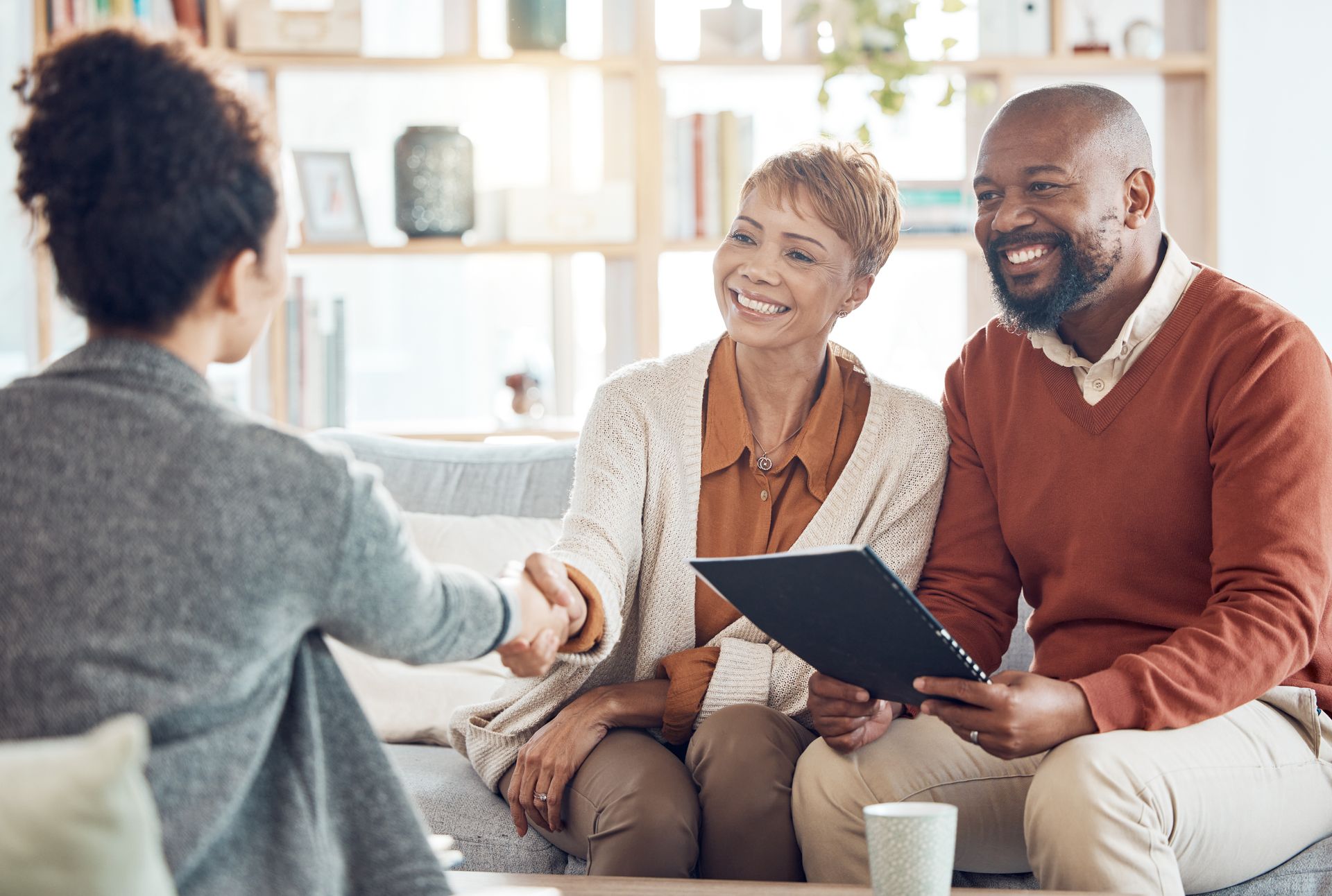 Two people smile and shake hands with a professional in a brightly lit office setting.