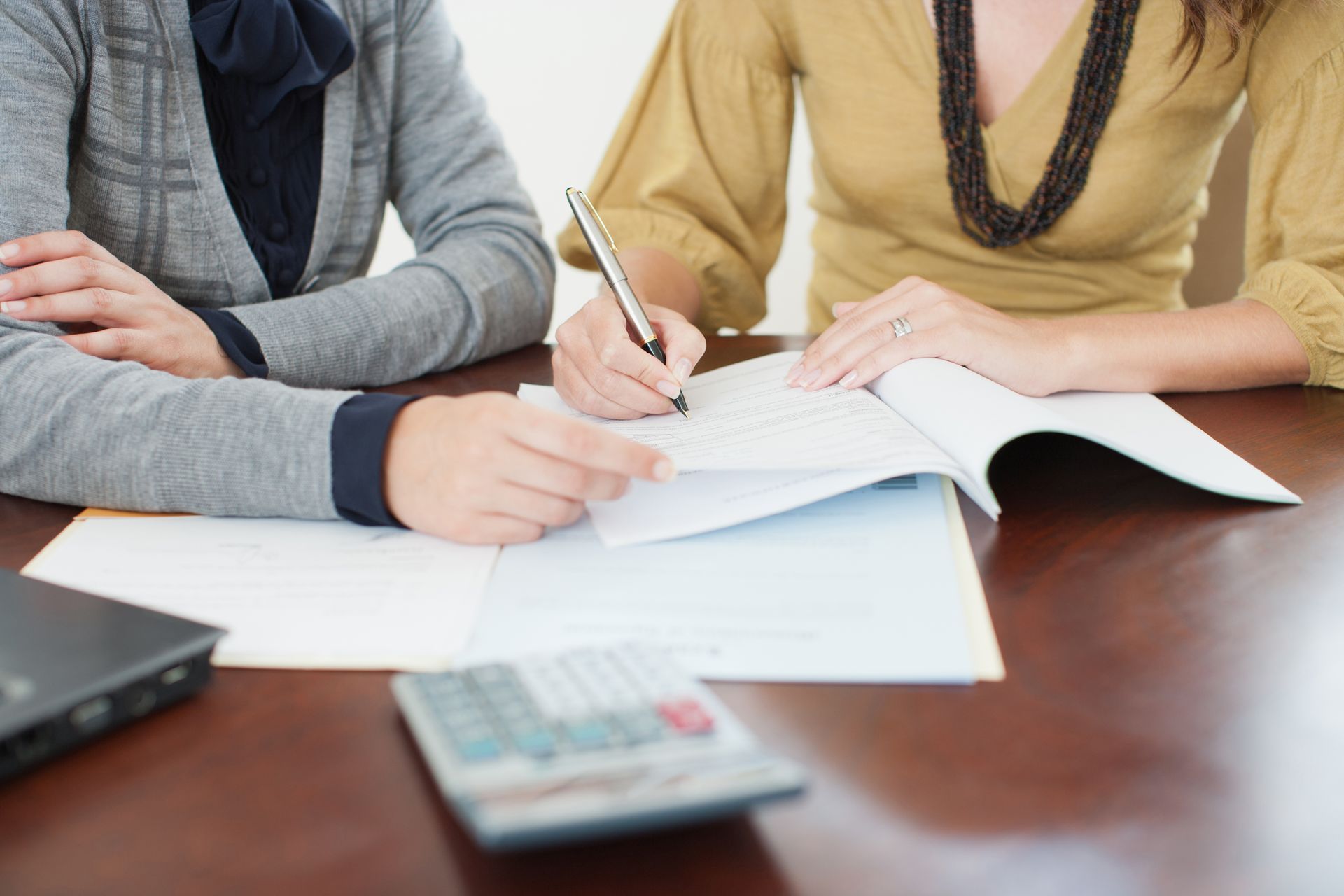 Two people sitting at a table with documents, a calculator, and a pen, collaborating on paperwork.