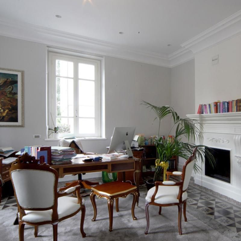 Elegante ufficio con scrivania, sedie, camino, finestra e pianta. Pareti grigie, pavimento a motivi.