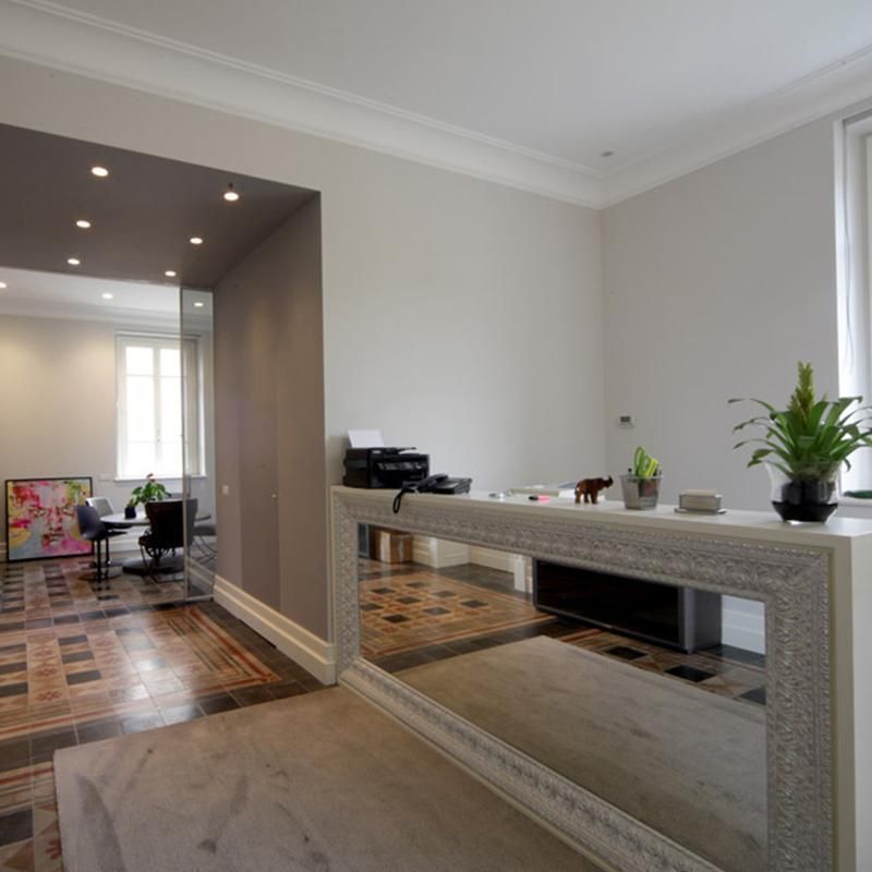 Ampio ufficio interno con un grande specchio, una stampante e uno scorcio di un'altra stanza con zona salotto.