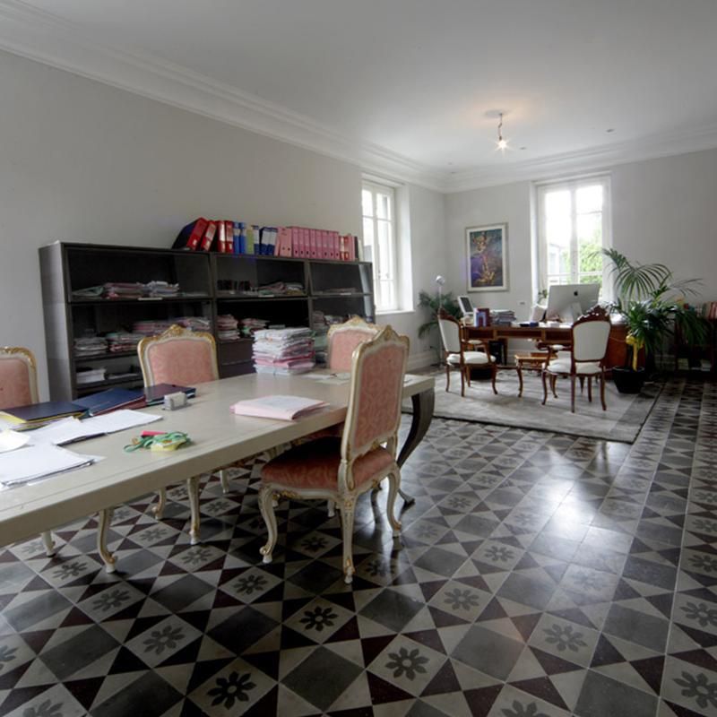 Ufficio con pavimento in piastrelle decorate, lungo tavolo con sedie, scrivania e schedari.