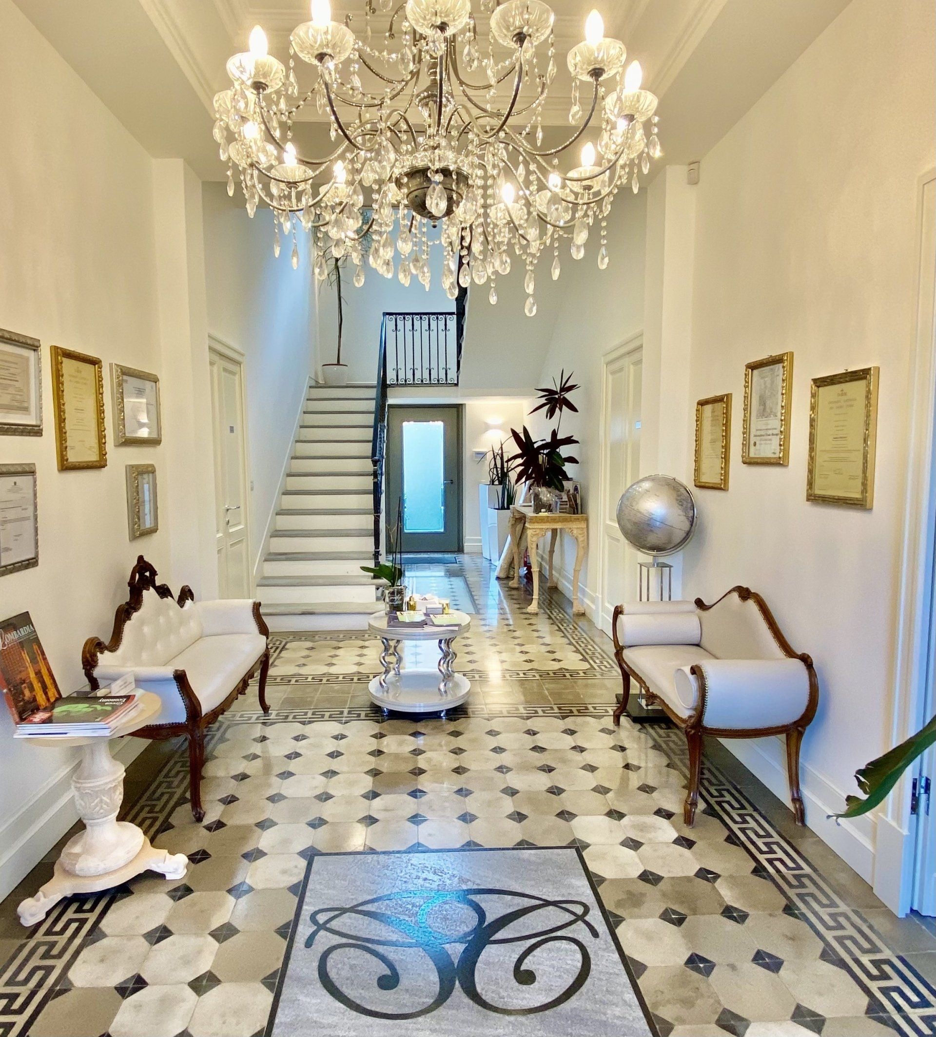 Elegante corridoio con lampadario decorato, scala in marmo e mobili antichi.