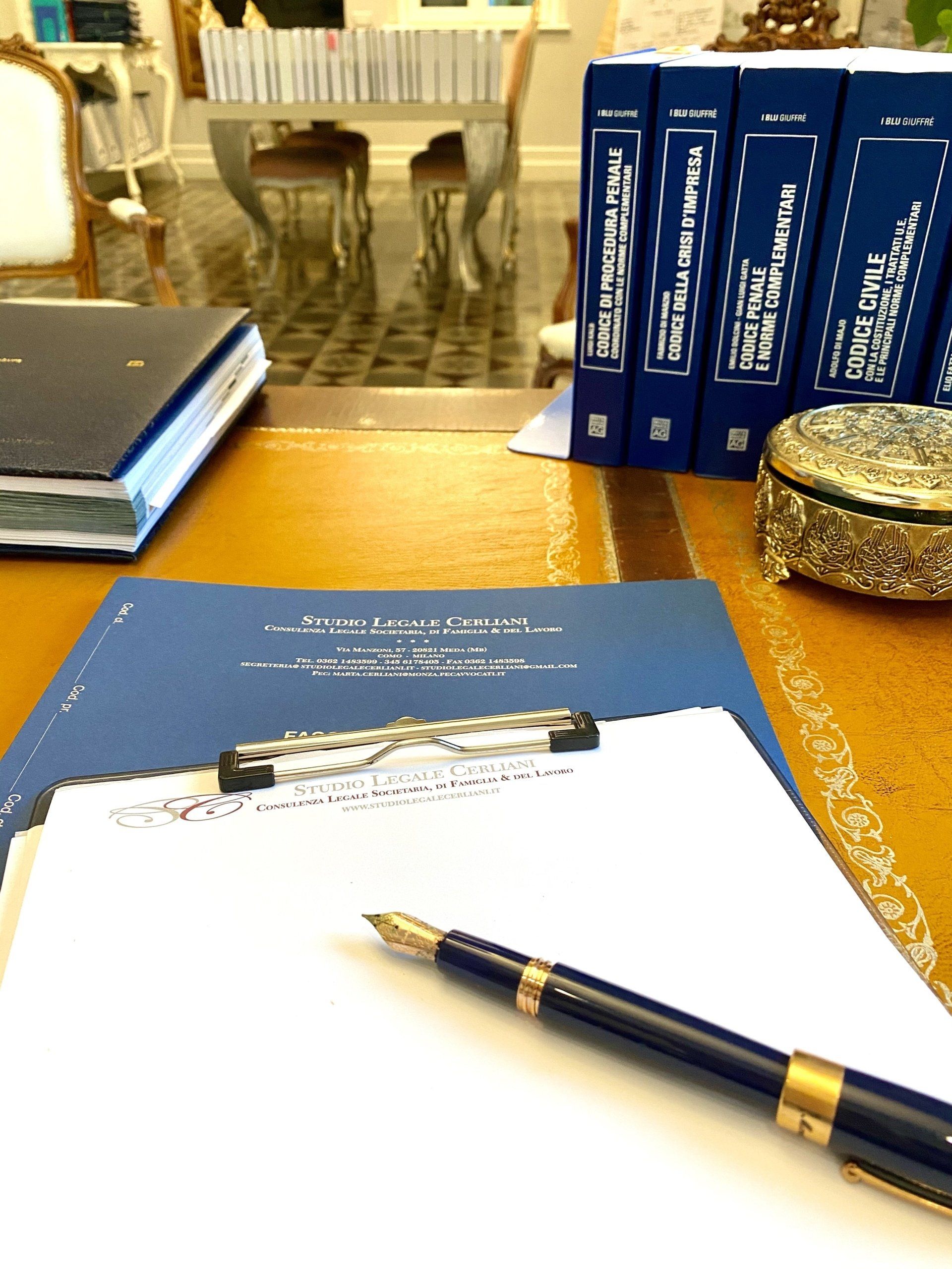 Una scrivania con documenti, penne e libri; l'attenzione è rivolta a un documento con una penna stilografica.