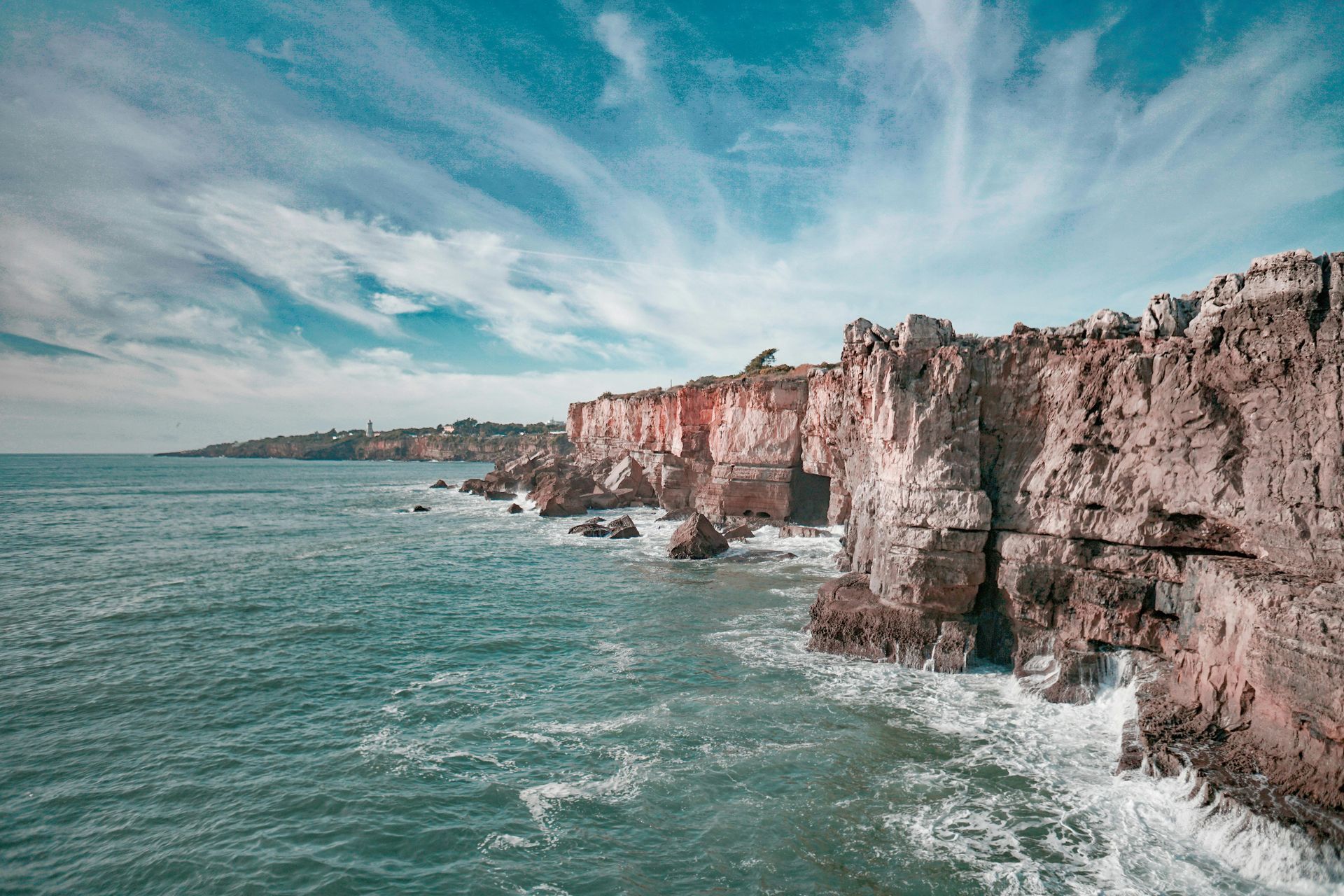 A cliff overlooking the ocean with waves crashing against it.