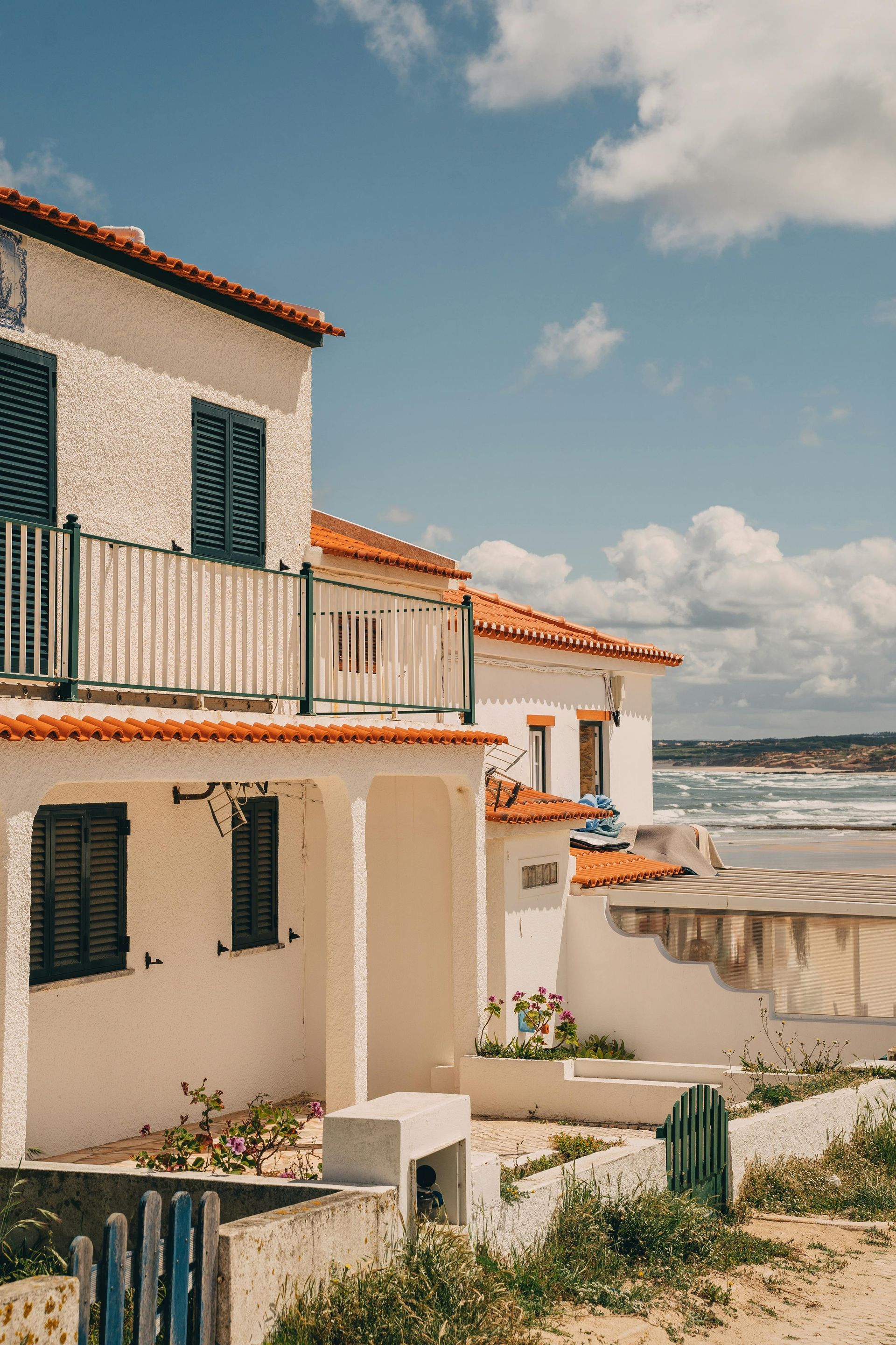 A white house with a balcony next to the ocean.