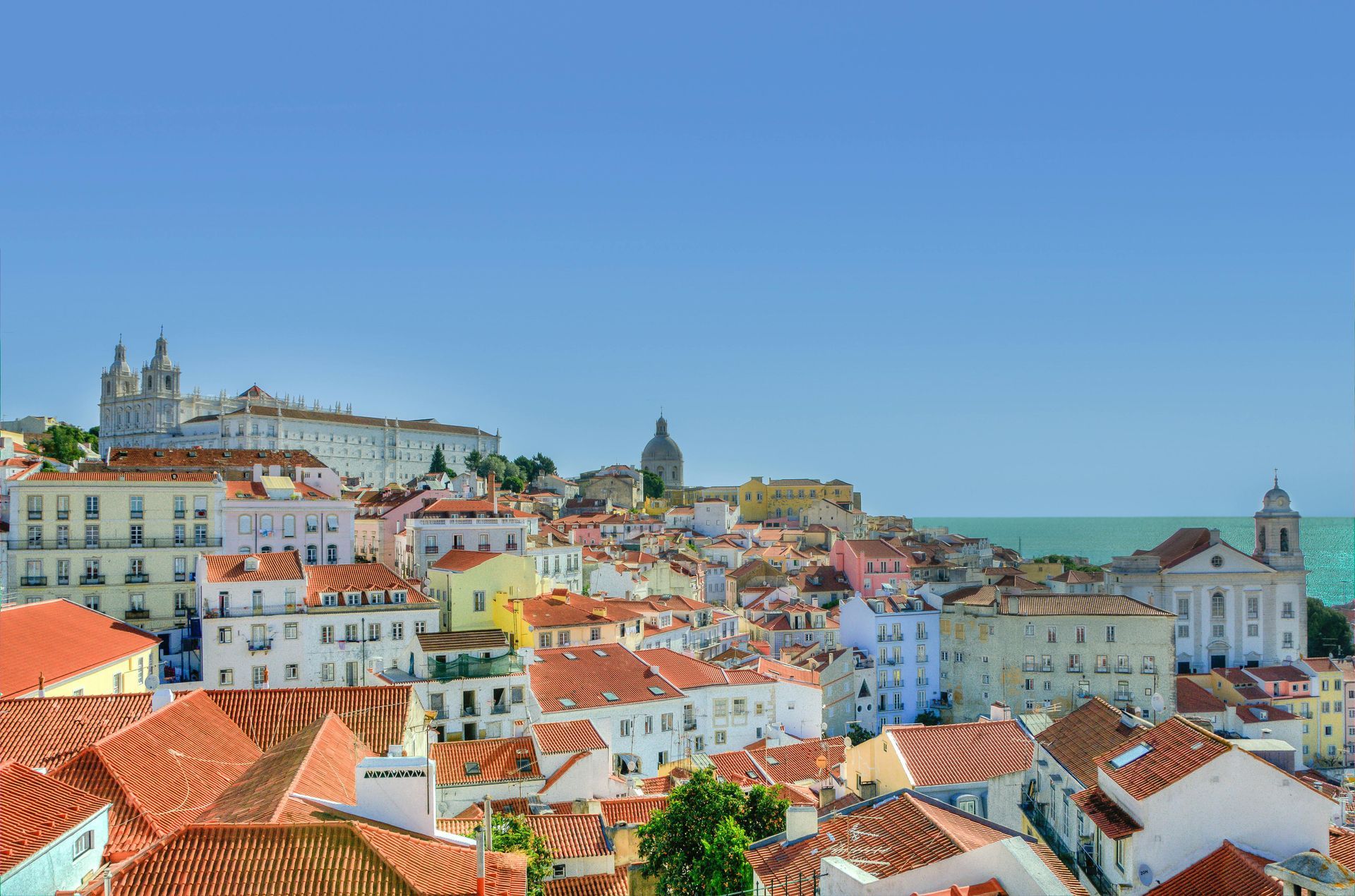 An aerial view of a city with red tiled roofs and the ocean in the background.