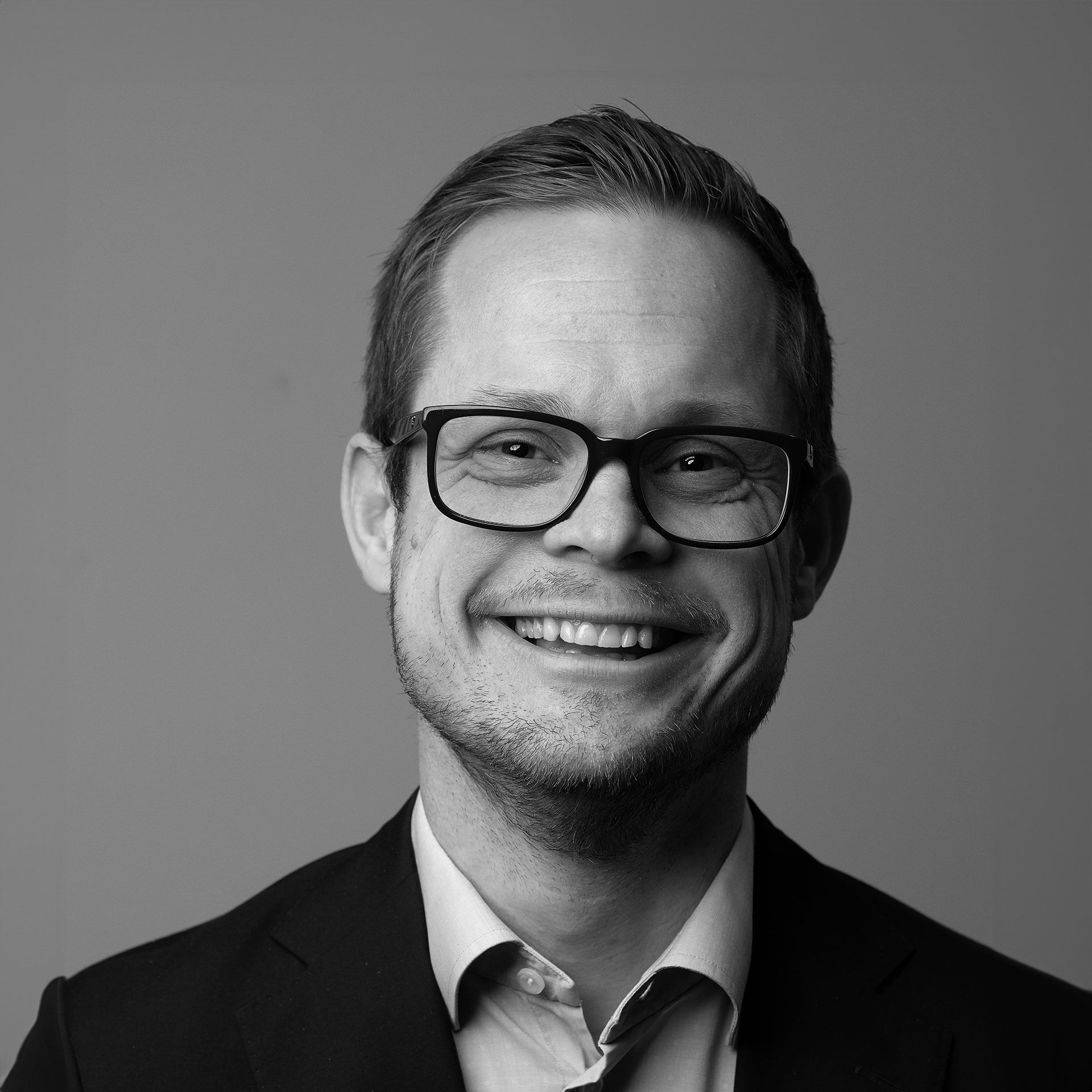 A black and white photo of a man wearing glasses and a jacket.