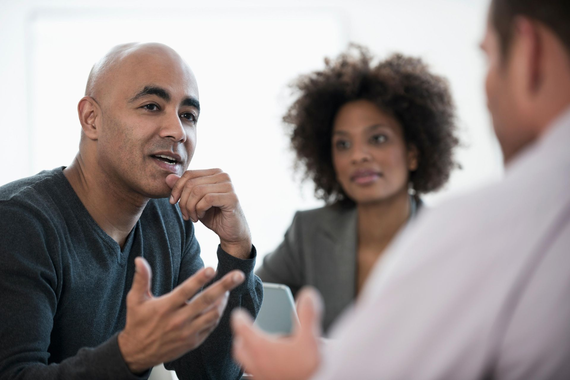 Man speaking, gesturing during meeting with two colleagues in office.