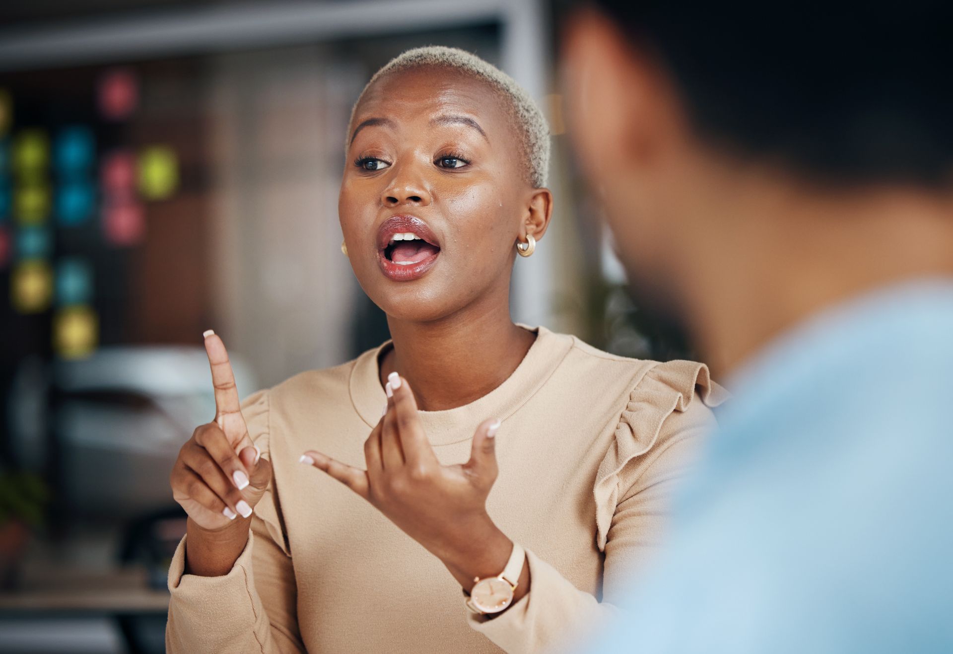 Woman with blonde hair gesturing while talking to a man in a well-lit room.