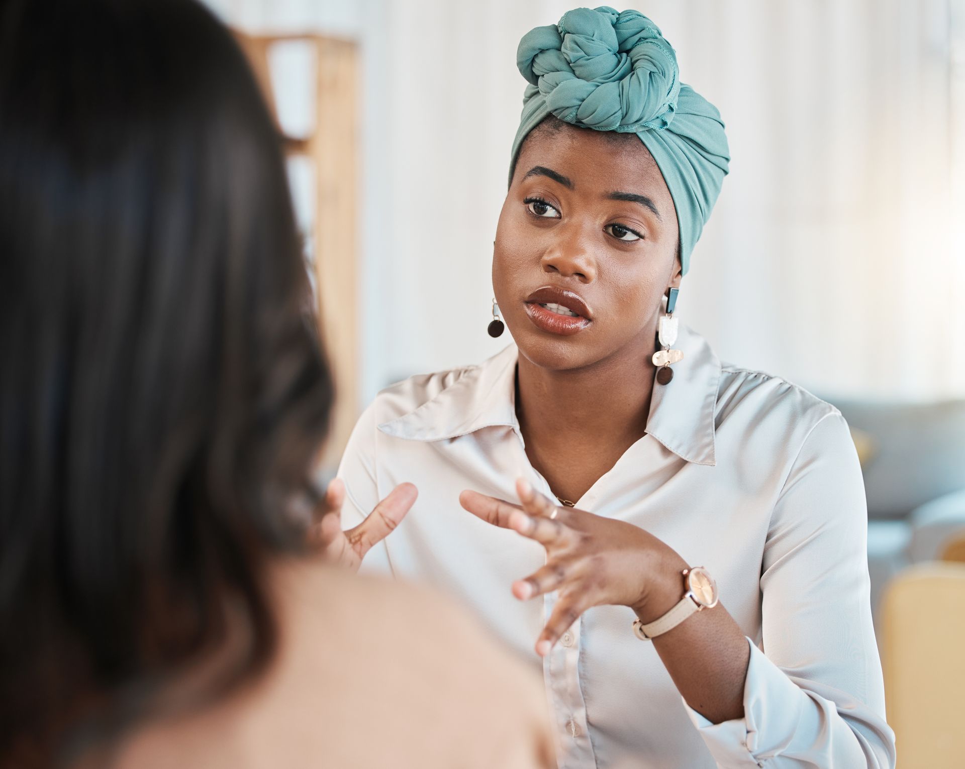 Woman and teen in therapy session. Woman gestures while speaking, teen listens with hand on face.