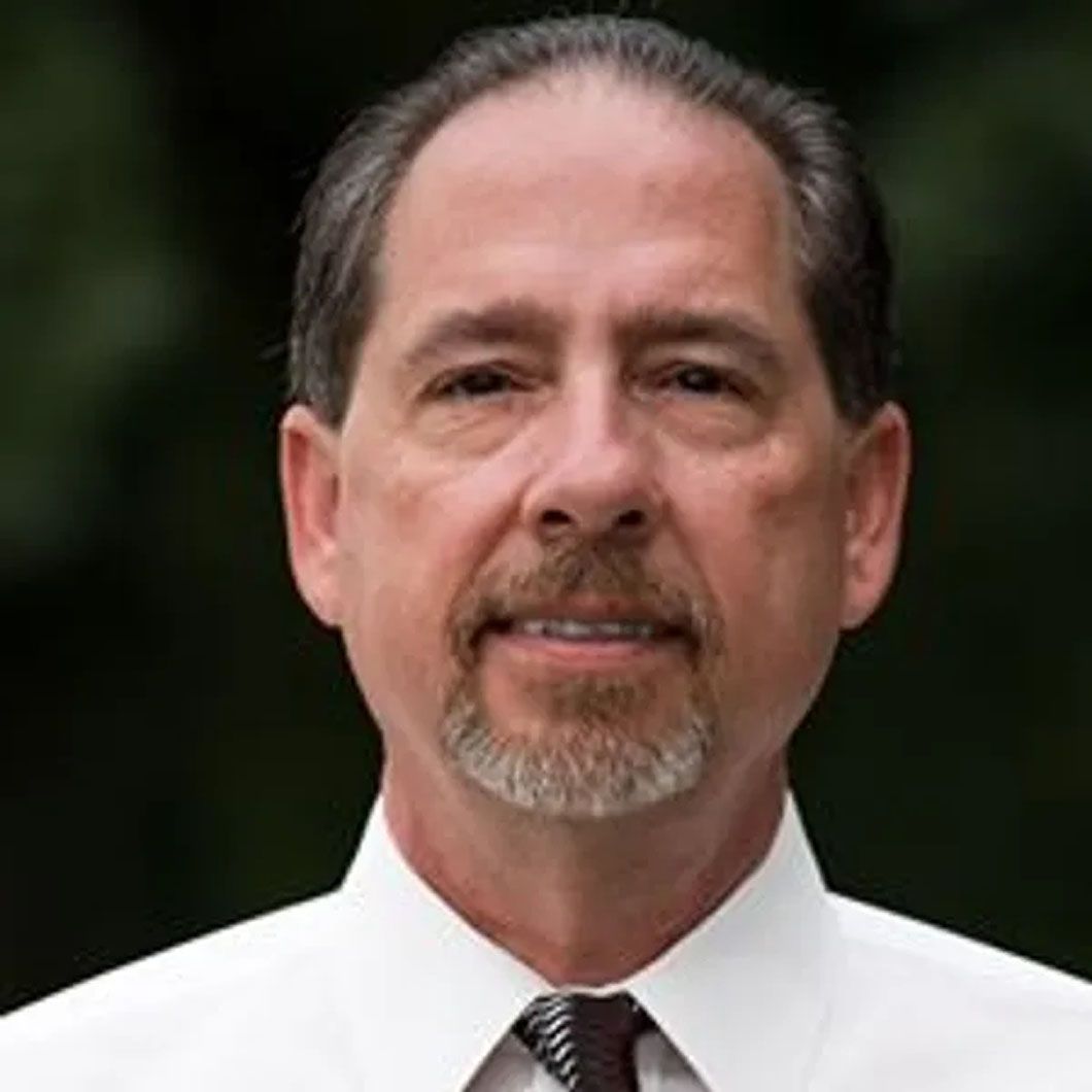 A man with a beard is wearing a white shirt and tie.