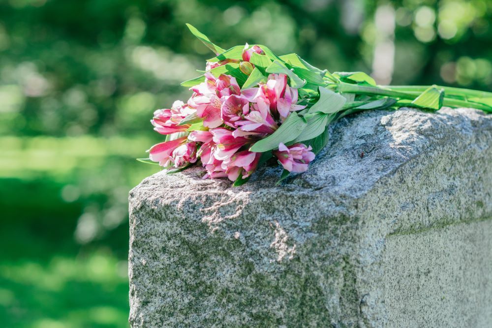 A bouquet of pink flowers is sitting on a gravestone.