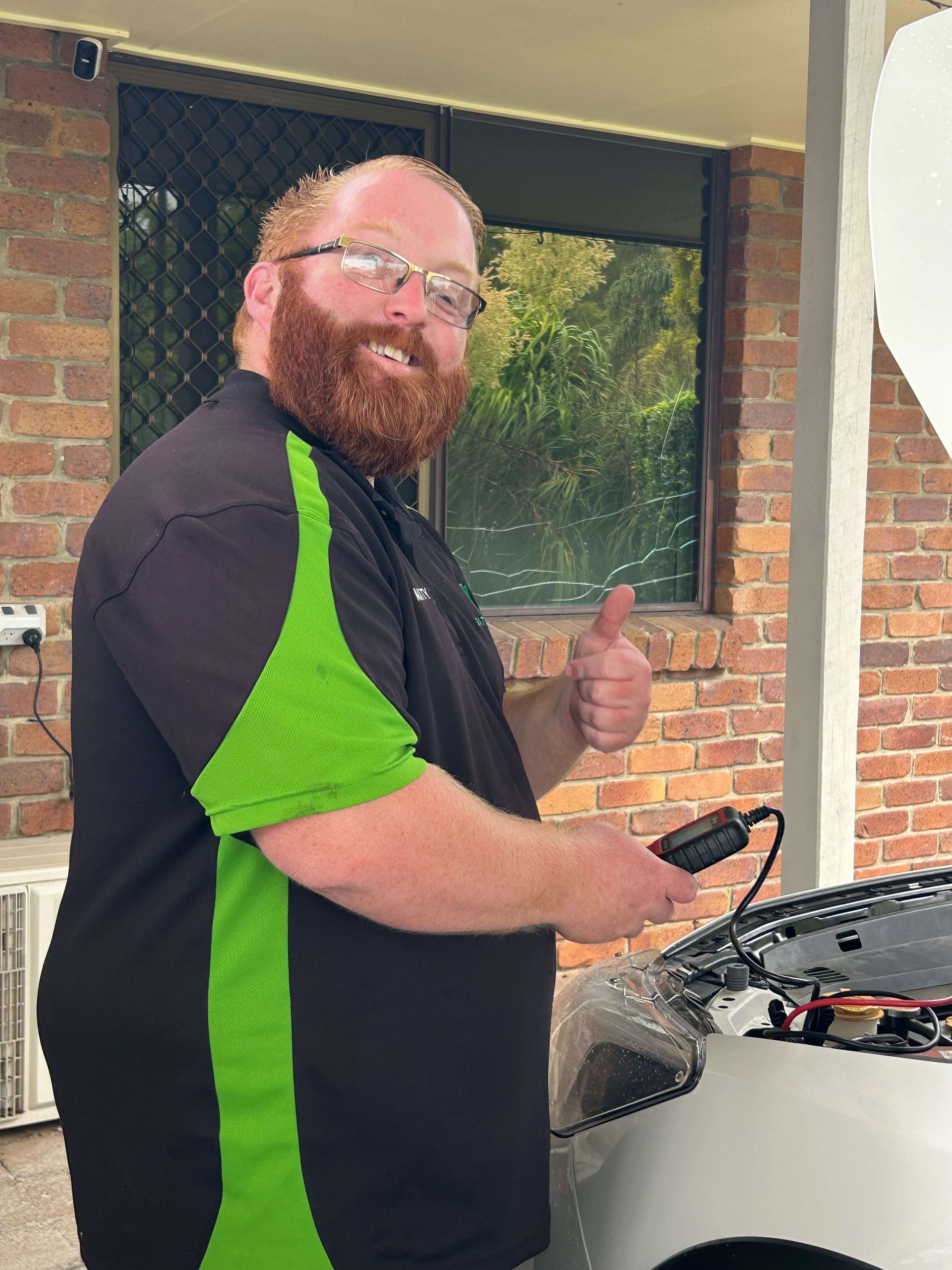 Mechanic holding device near car engine, giving thumbs up. Wearing black shirt with green — Battery Assist Brisbane in Caboolture, QLD
