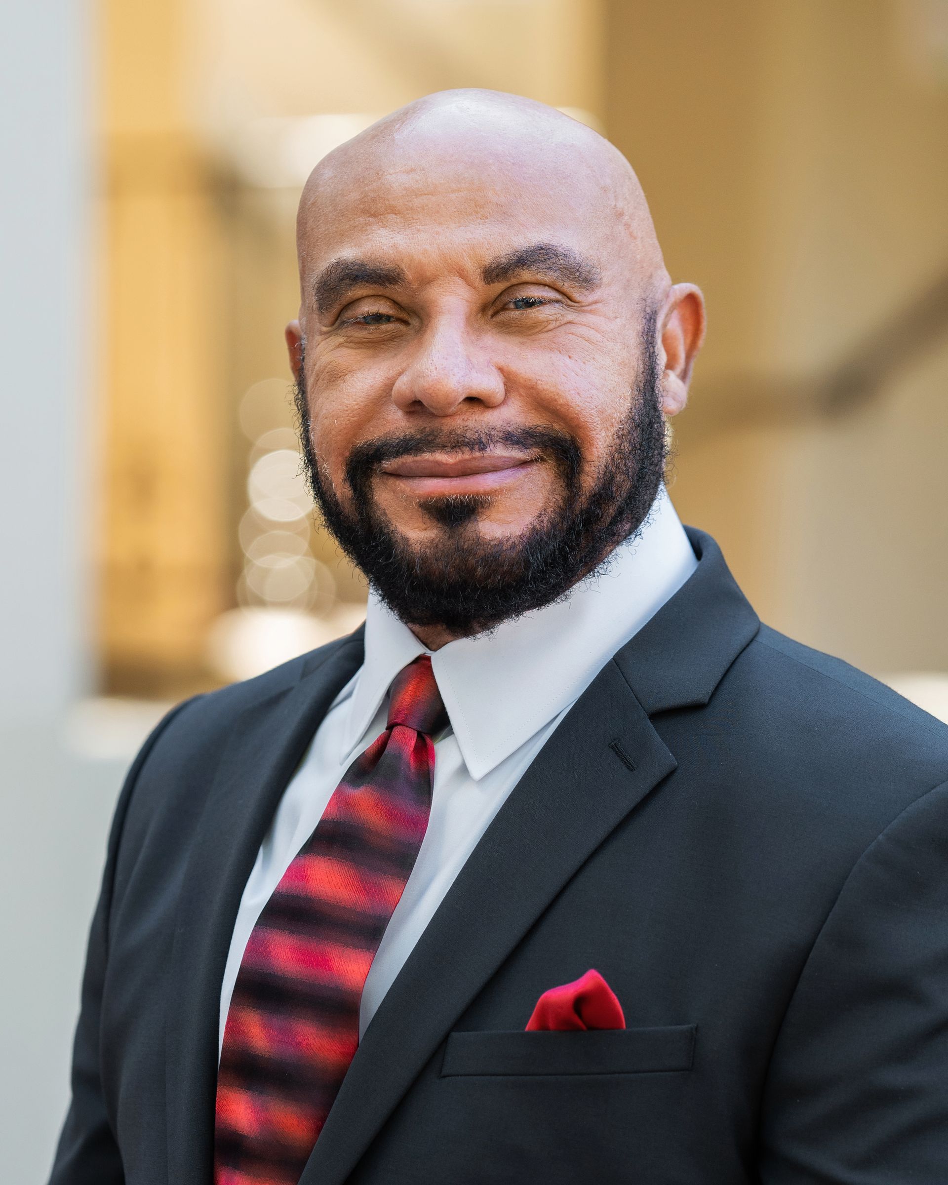 A bald man with a beard is wearing a suit and tie.