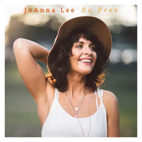 A woman wearing a hat and a white tank top is smiling.