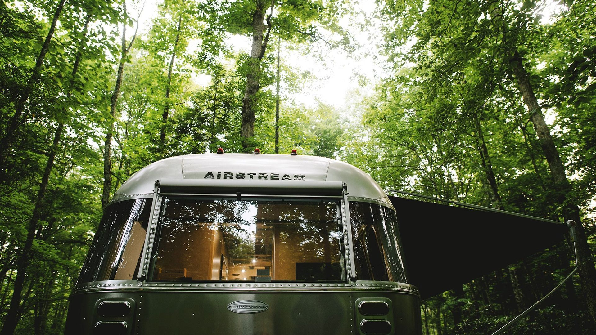 An airstream trailer is parked in the middle of a forest.