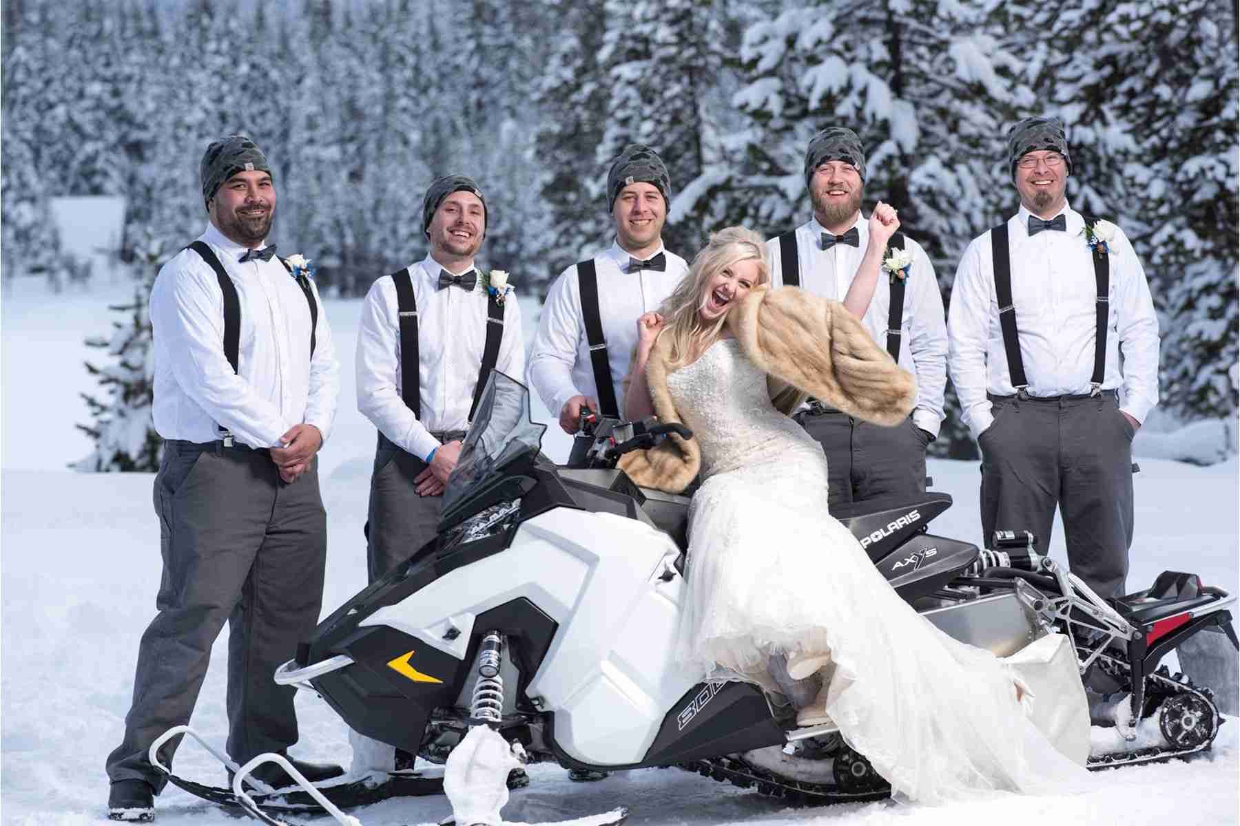A bride and her groomsmen are posing for a picture with a snowmobile.