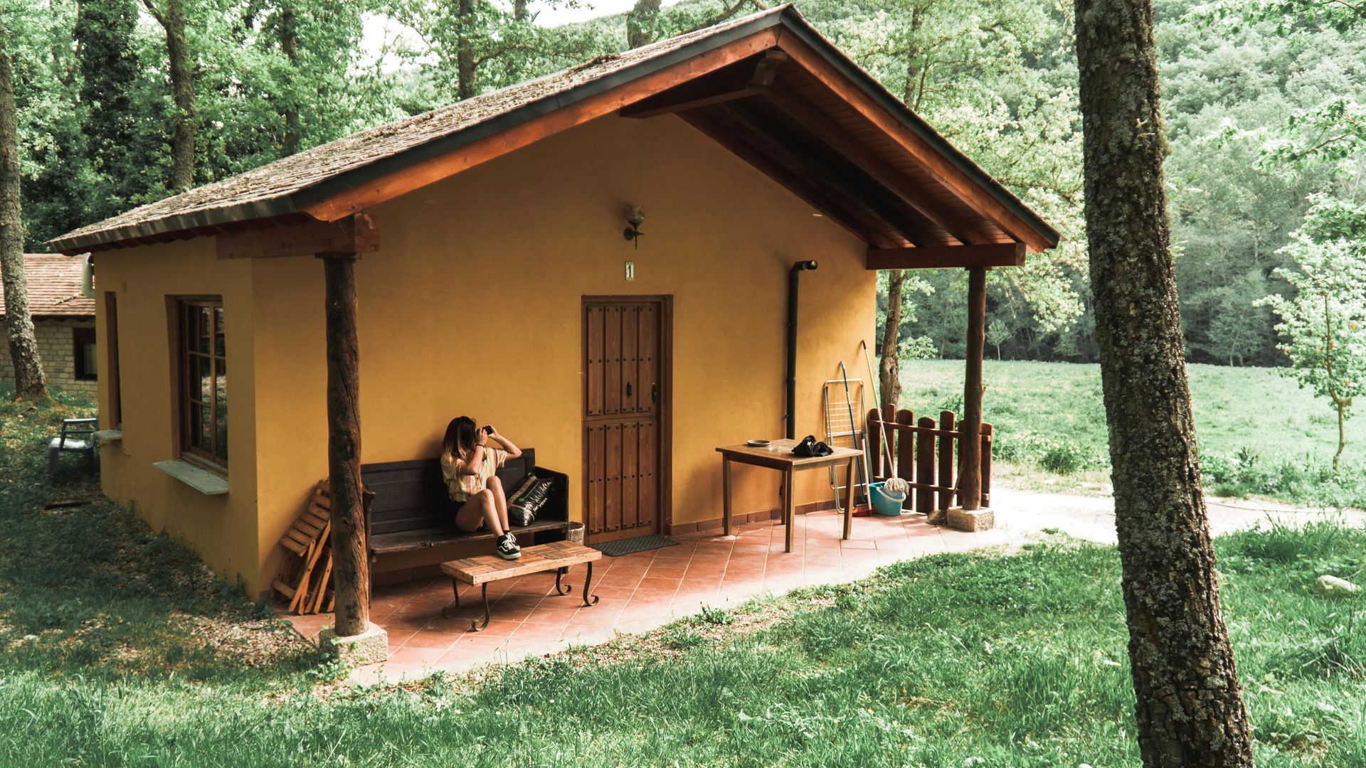 A woman is sitting on a bench on the porch of a small house.