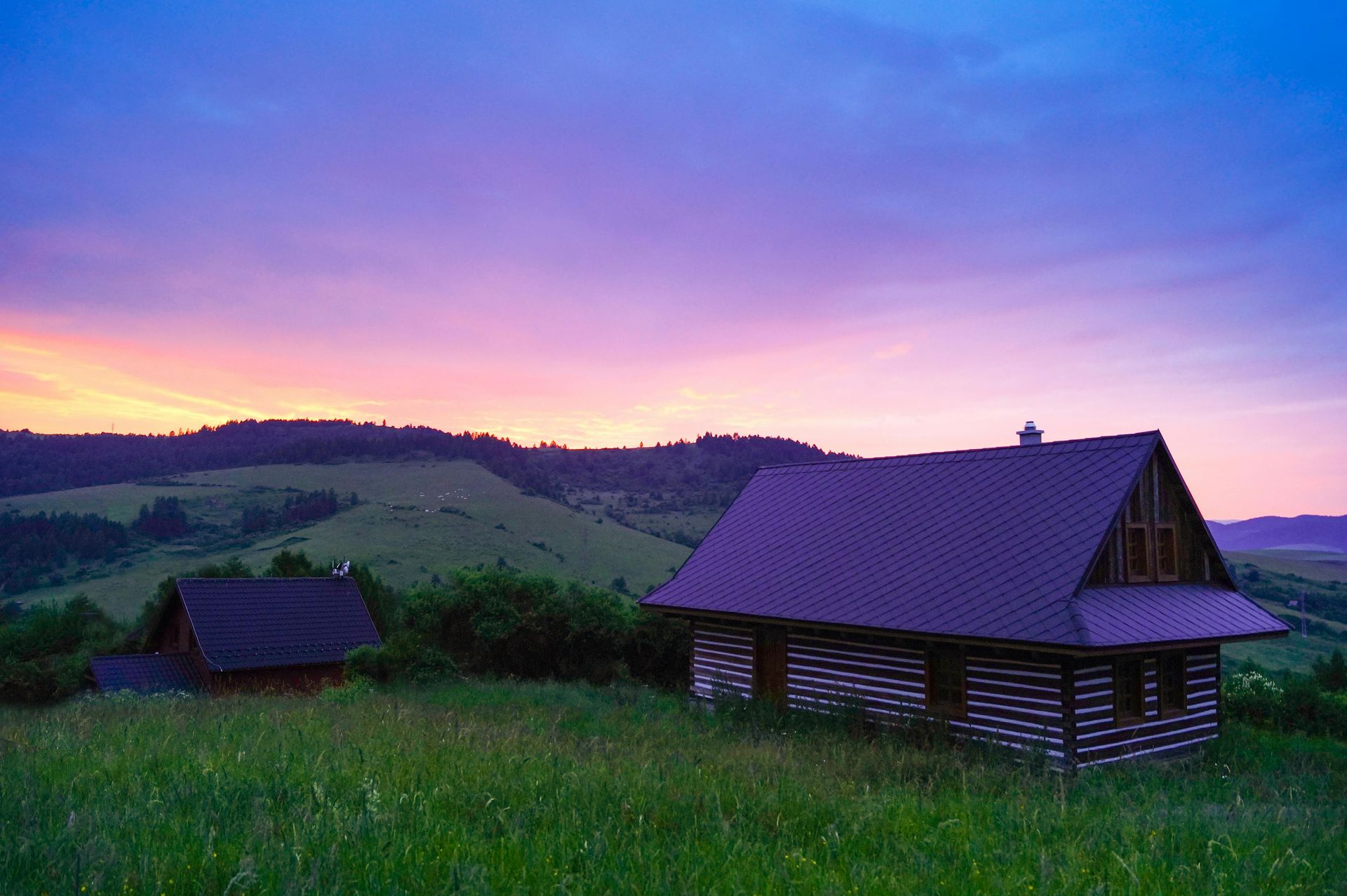 A couple of houses sitting on top of a grassy hill at sunset.